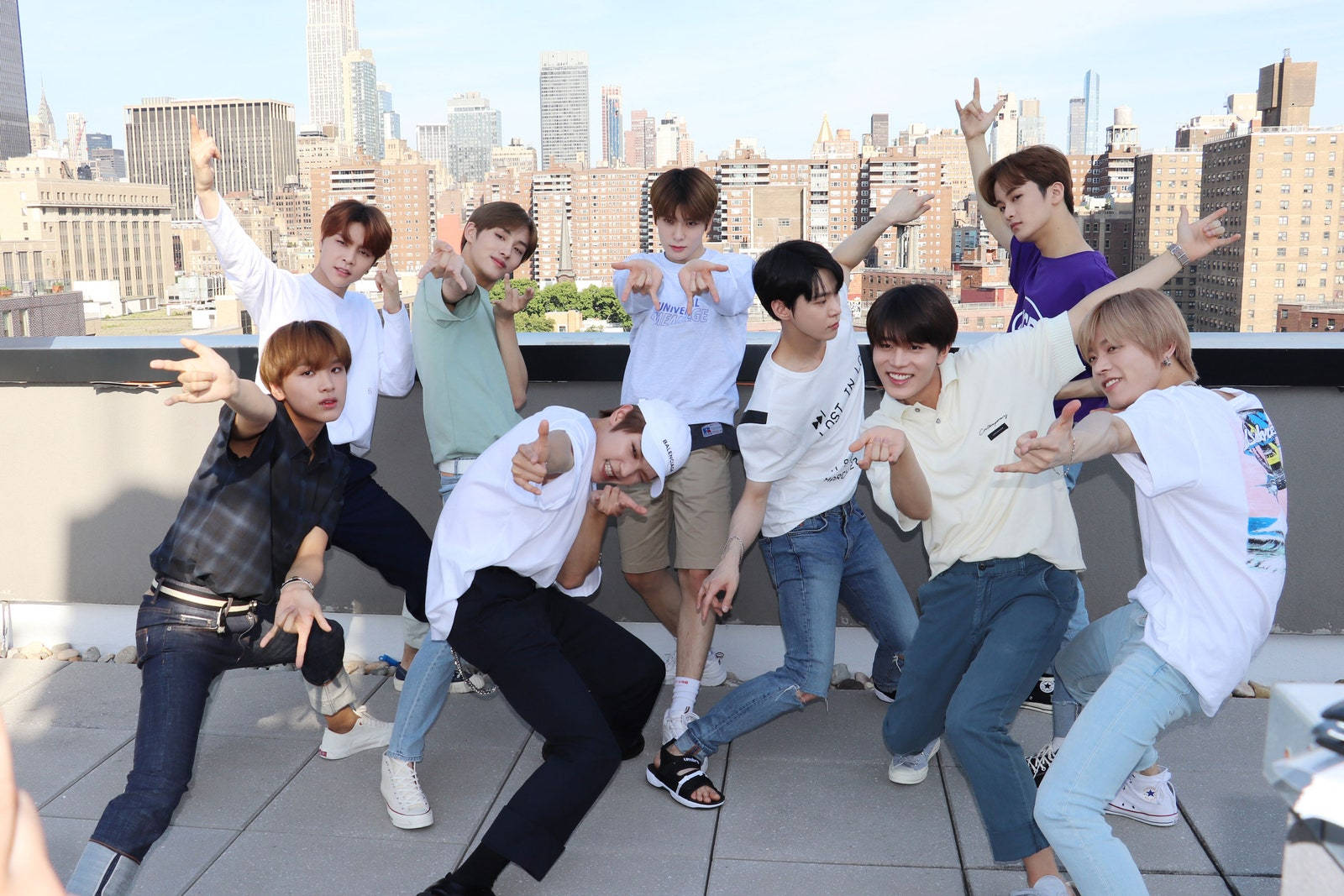NCT 127蜘蛛人姿勢 壁紙 — 七個年輕男子在屋頂上擺出充滿動感的舞蹈姿勢，背後是廣闊的城市天際線，在明亮的日光下。