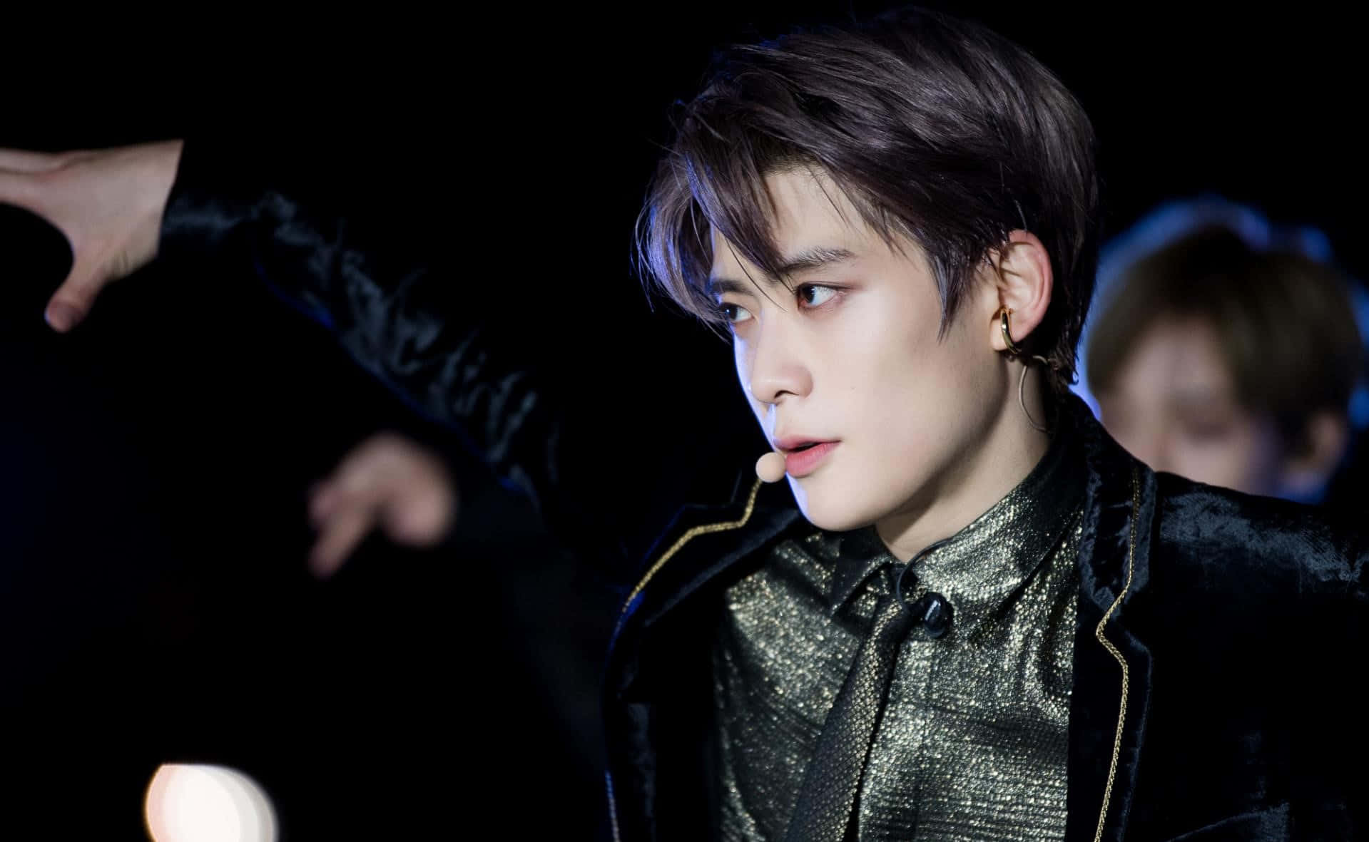 NCT Jaehyun 舞蹈瞬間 壁紙 — 一位男性表演者身穿黑色天鵝絨外套，飾有金色滾邊和閃亮襯衫，在舞台燈光下做出戲劇性的手勢。