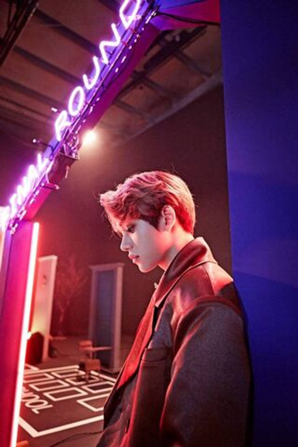 NCT Lucas 墙壁 壁紙 — 一位紅髮年輕男子在昏暗的房間裡，在發光的霓虹燈下靠著牆。