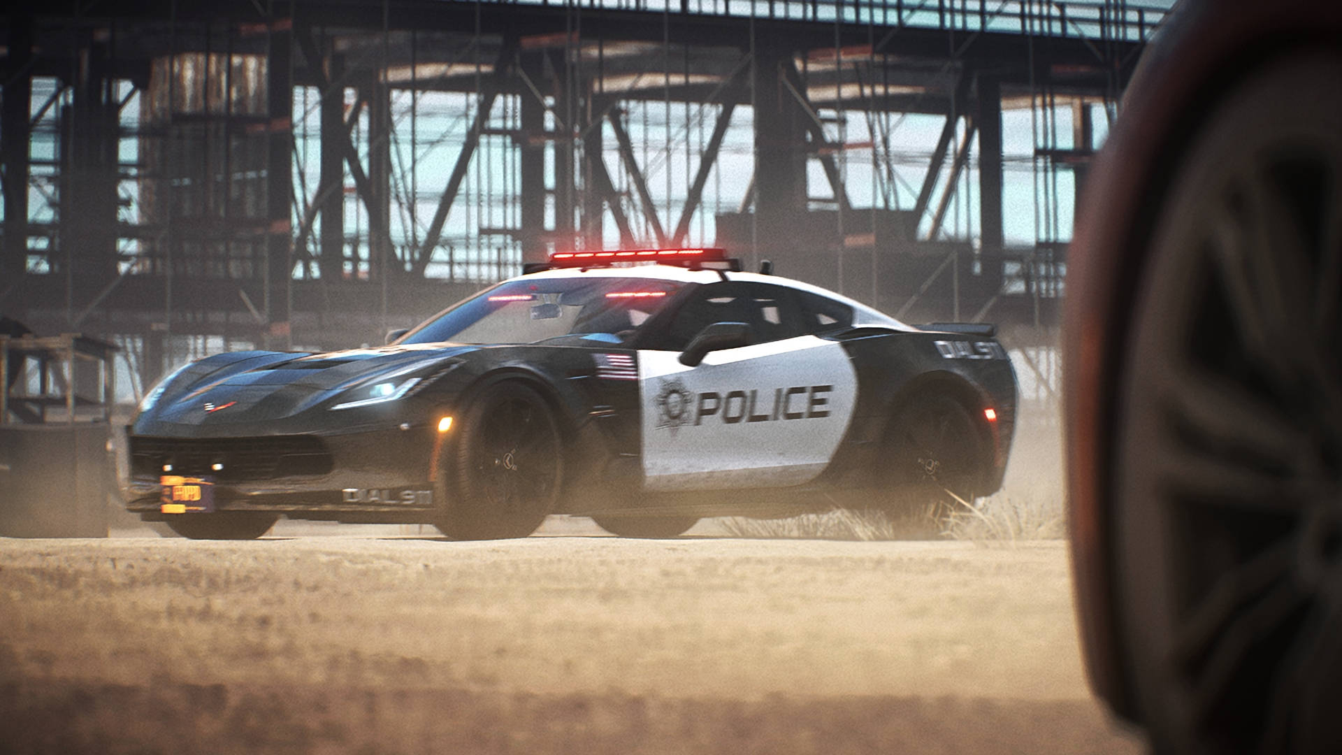 《Need for Speed Payback》警察追捕 壁紙 — 一輛黑白警用Corvette在巨大的鋼橋下，伴隨著閃爍的紅燈，在塵土飛揚的地形上疾馳。