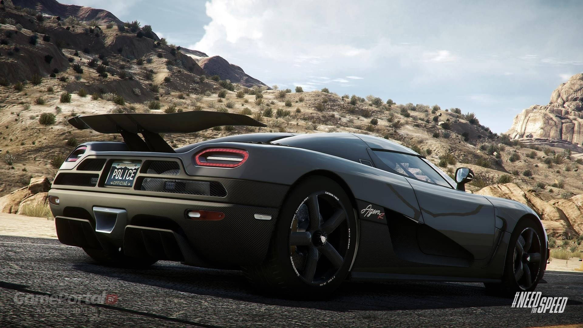 《Need For Speed Rivals》黑色Koenigsegg Agera R警車後視圖 壁紙 — 一輛時尚的啞光灰色 Koenigsegg Agera R 警車，展開後翼，在晴朗天空下沿著沙漠公路疾馳，兩旁是岩石丘陵。