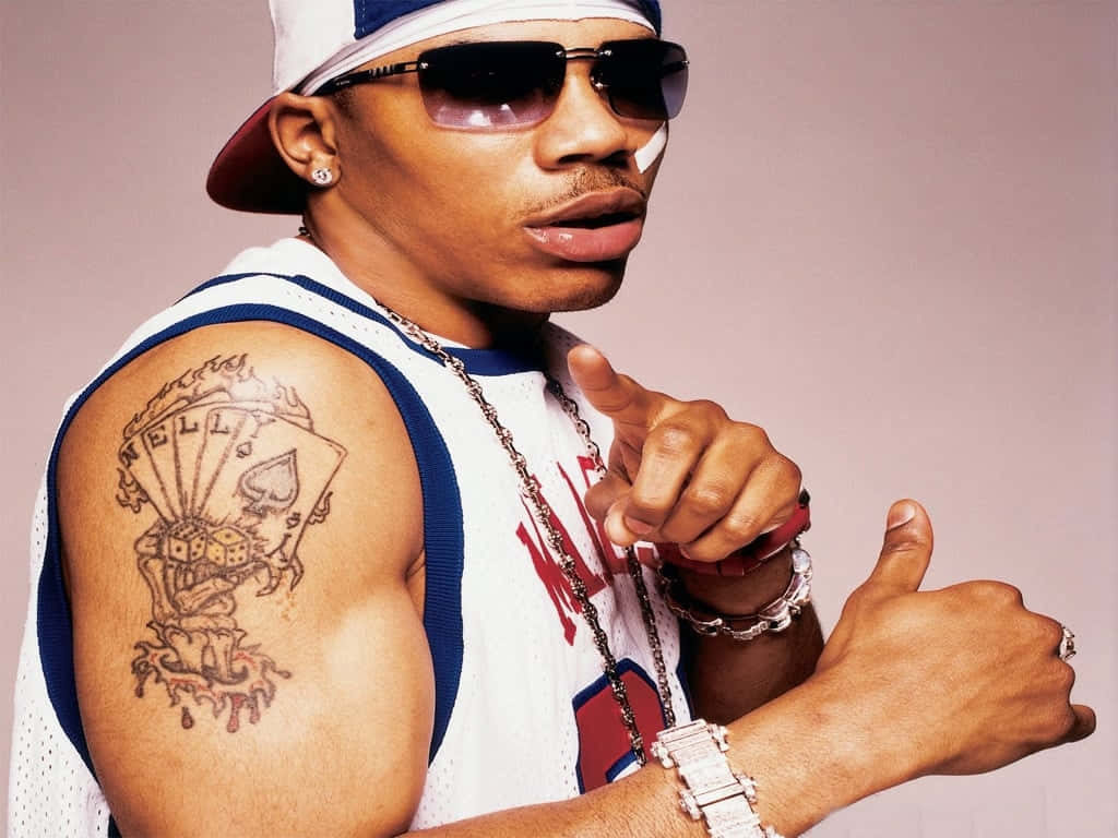 Nelly《Country Grammar》音樂錄影帶 壁紙 — 一個身穿籃球球衣和戴帽子的男人自信地指著，展示他手臂上精細的紋身。
