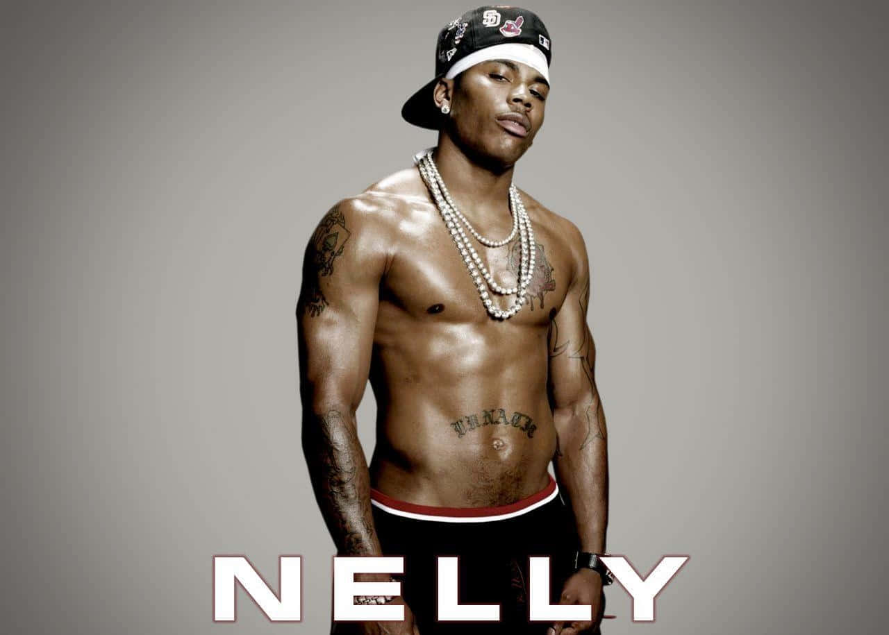 Nelly 無上衣展現堅毅神情 壁紙 — 赤裸上身的Nelly，帶有紋身和珍珠項鍊，在純灰色背景前自信地擺姿勢。