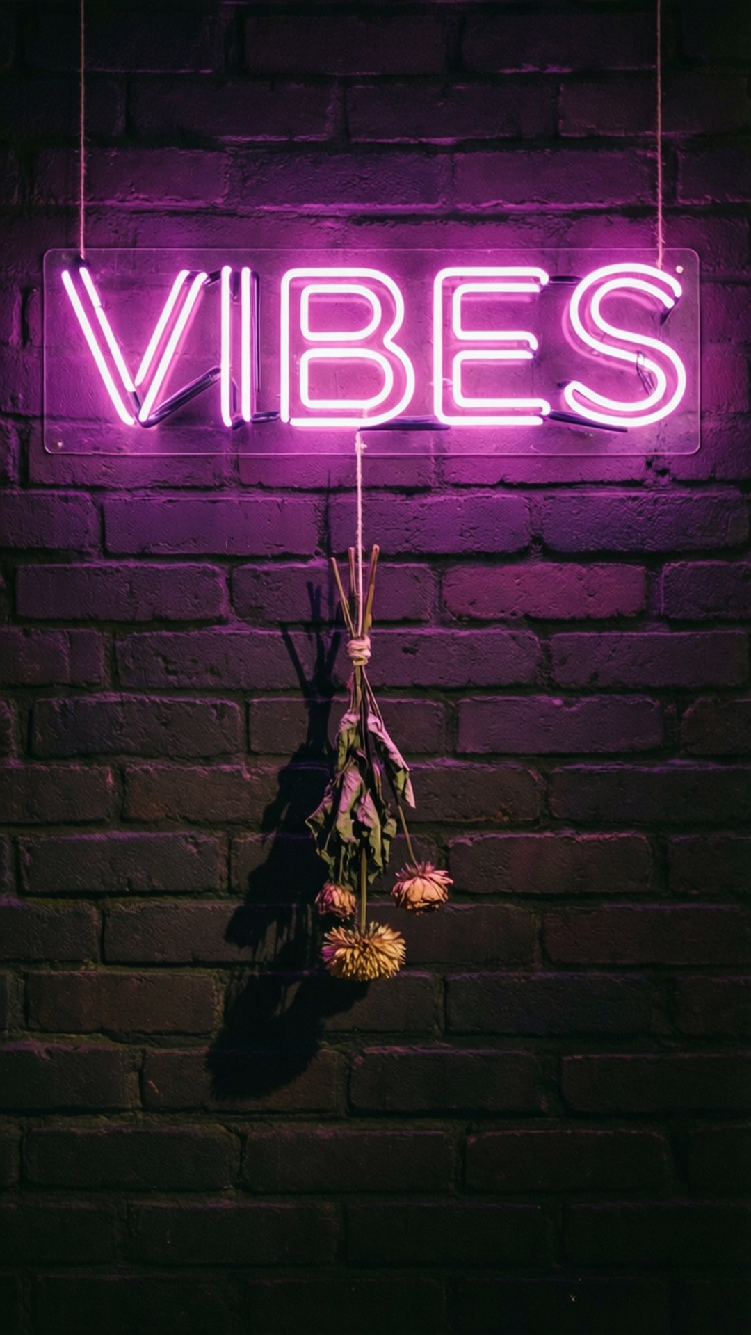 粉紅色霓虹燈牌寫著 vibes 掛在磚牆上，下方有乾花