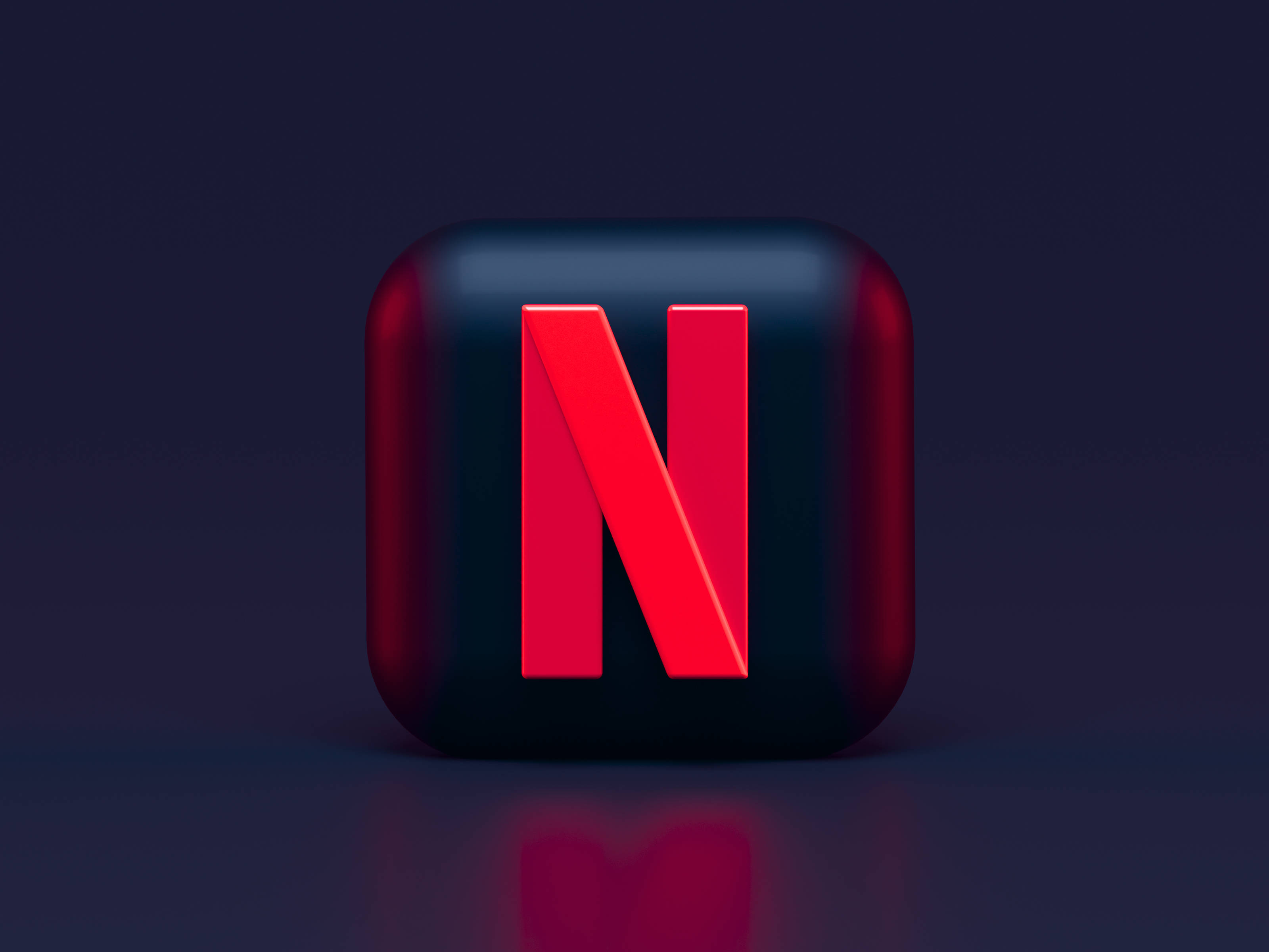 Netflix 3D立方體 壁紙 — 一個光澤的黑色立方體，帶有醒目的紅色Netflix標誌，在工作室燈光下居中放置在深色反光表面上。