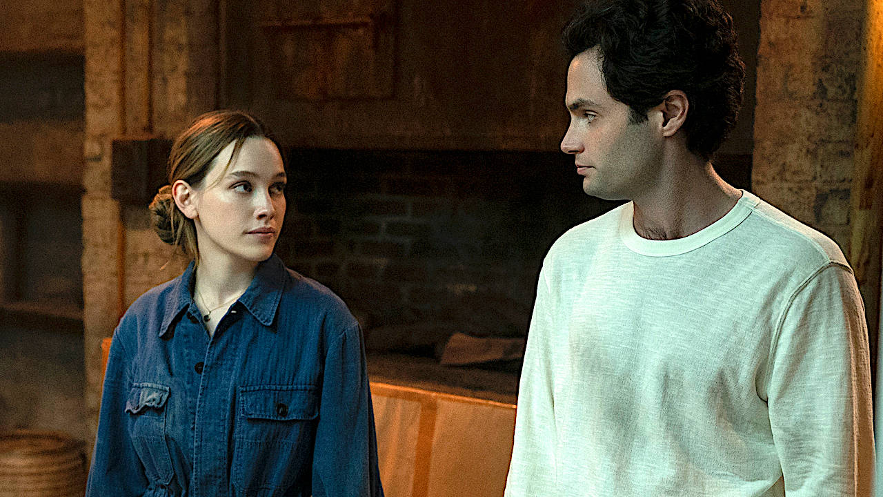 Netflix《You》第三季喬與蘿莉場景 壁紙 — 一男一女站在一個有溫暖燈光和磚牆的質樸房間裡，專注地凝視著對方。