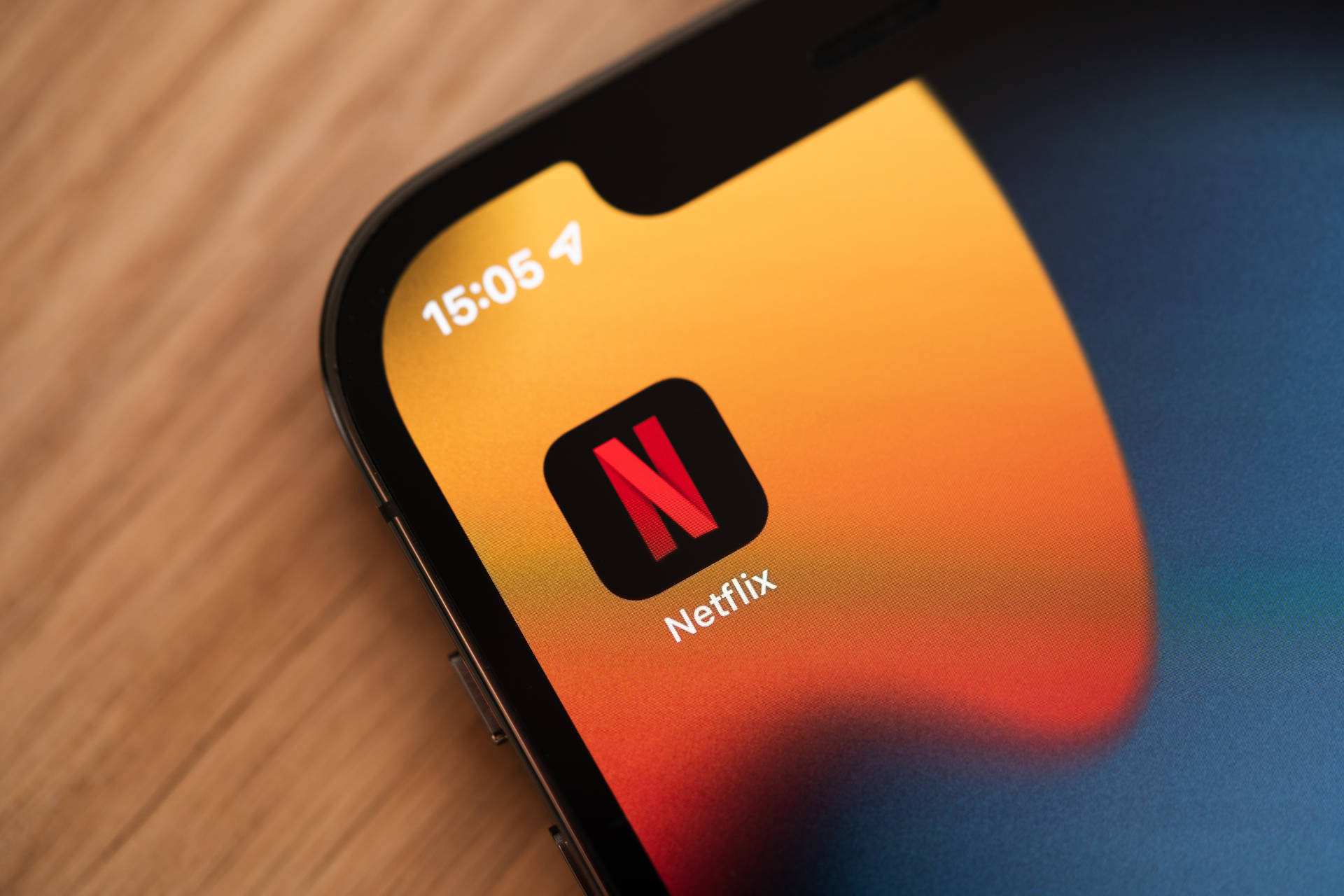 智能手機在木桌上顯示彩色漸變背景上的Netflix應用程式圖標。