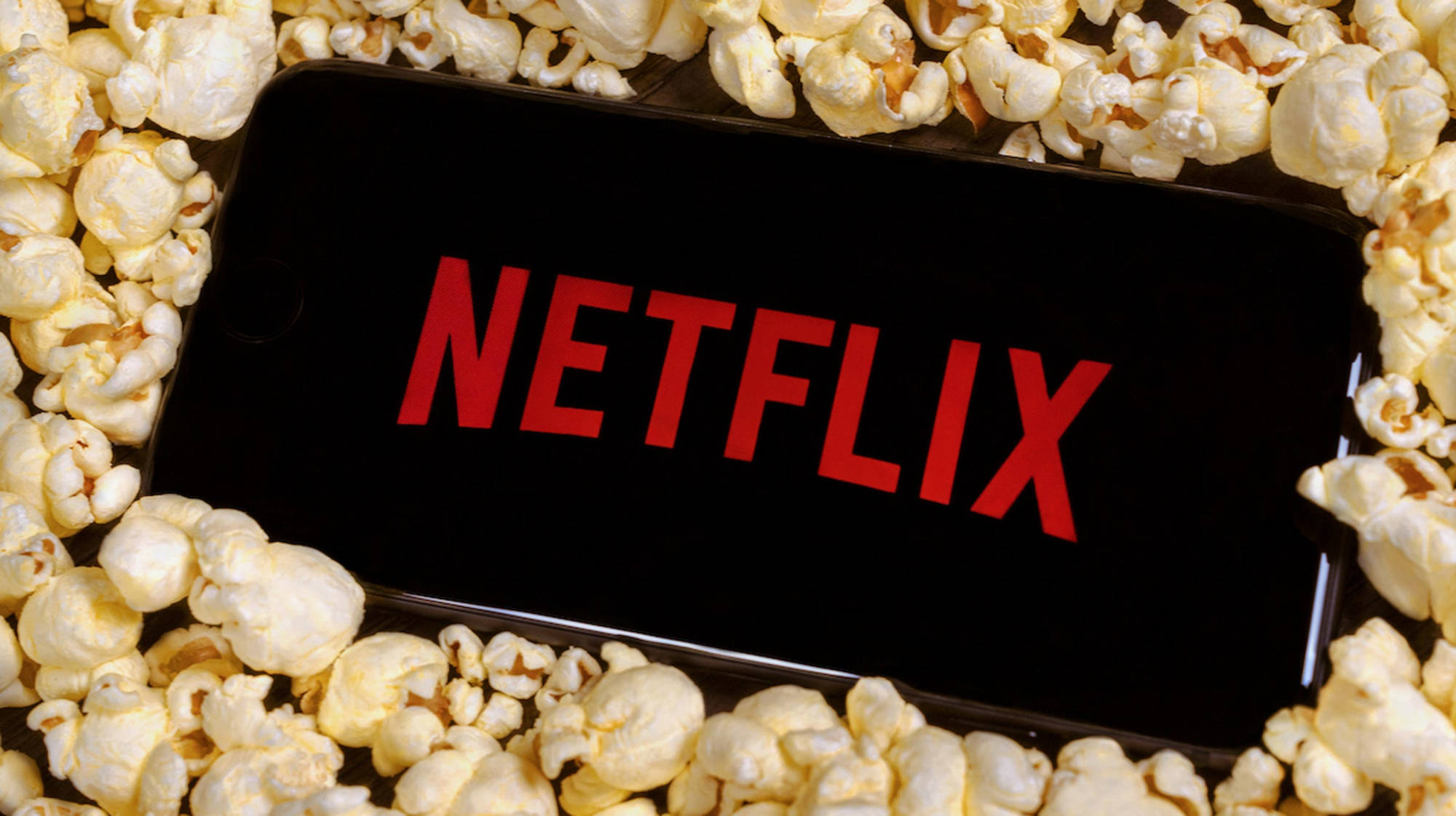 Netflix 風格爆米花 壁紙 — 一部顯示紅色 Netflix 標誌的智能手機，安放在一床鬆軟的白色爆谷中。
