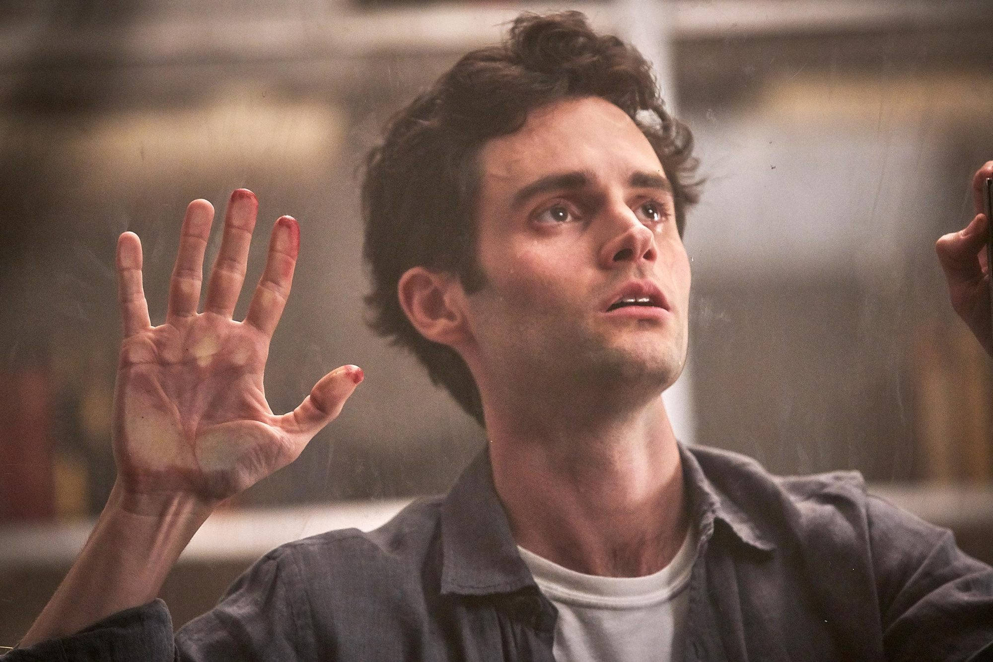 Netflix劇集《You》演員彭·巴德利 壁紙 — 一名深色頭髮的男子將雙手按在雨水打濕的窗戶上，雙眼因震驚或恐懼而睜大。