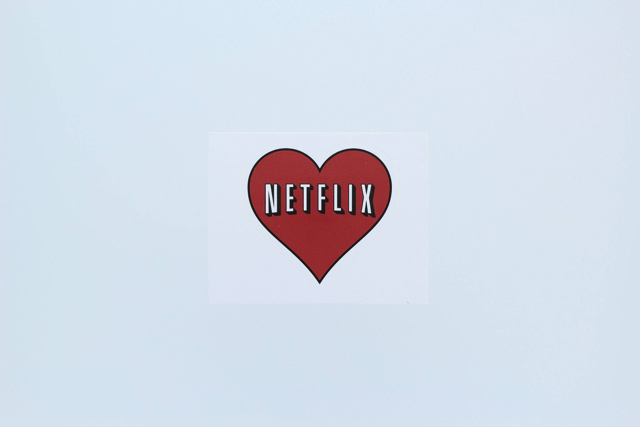 Netflix愛心圖案 壁紙 — 一個紅色心形Netflix標誌貼紙，置於純淺藍色背景中央。