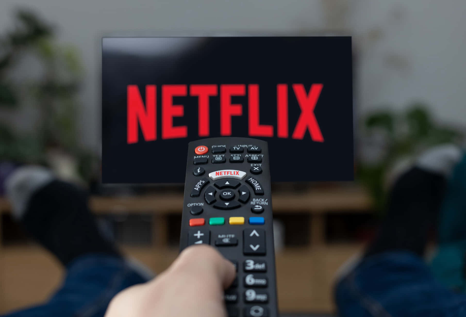 手拿遙控器指向客廳電視屏幕上的 Netflix 標誌。