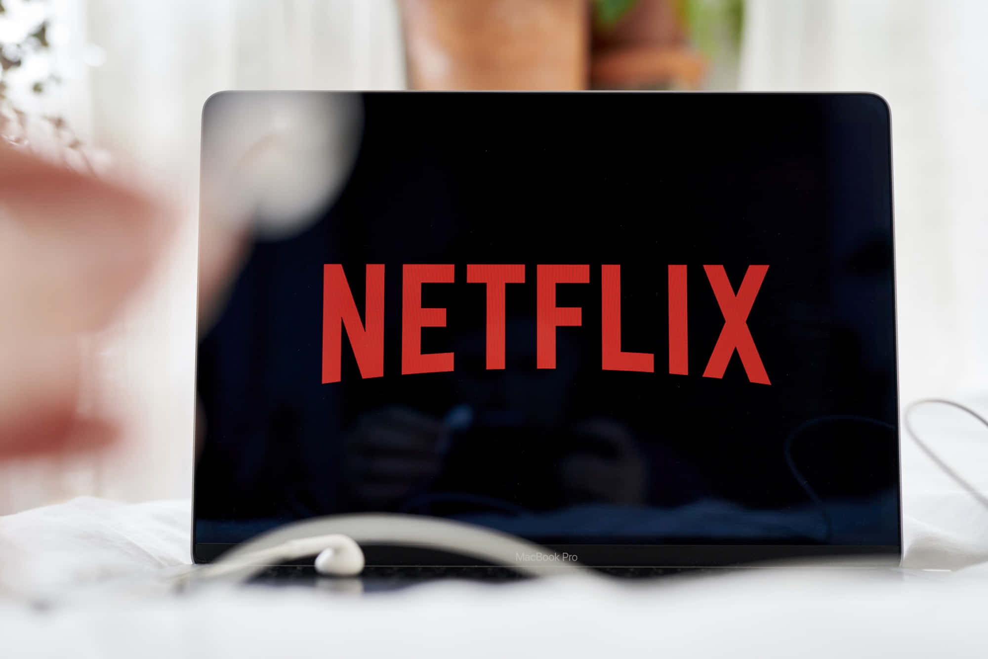筆記型電腦顯示Netflix標誌，耳機在附近白色表面上。
