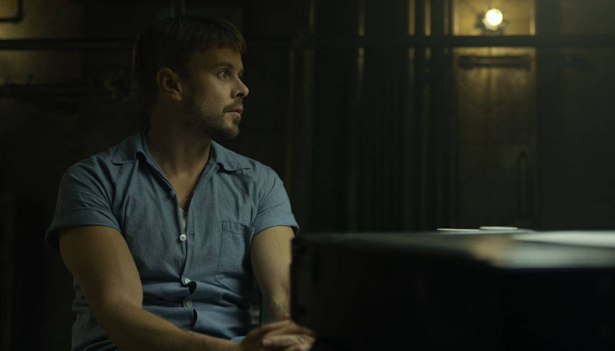 Netflix熱門劇集《Mindhunter》 壁紙 — 一名身穿藍色恤衫的男子在昏暗的房間裡，在溫暖的環境燈光下沉思地坐在鋼琴前。