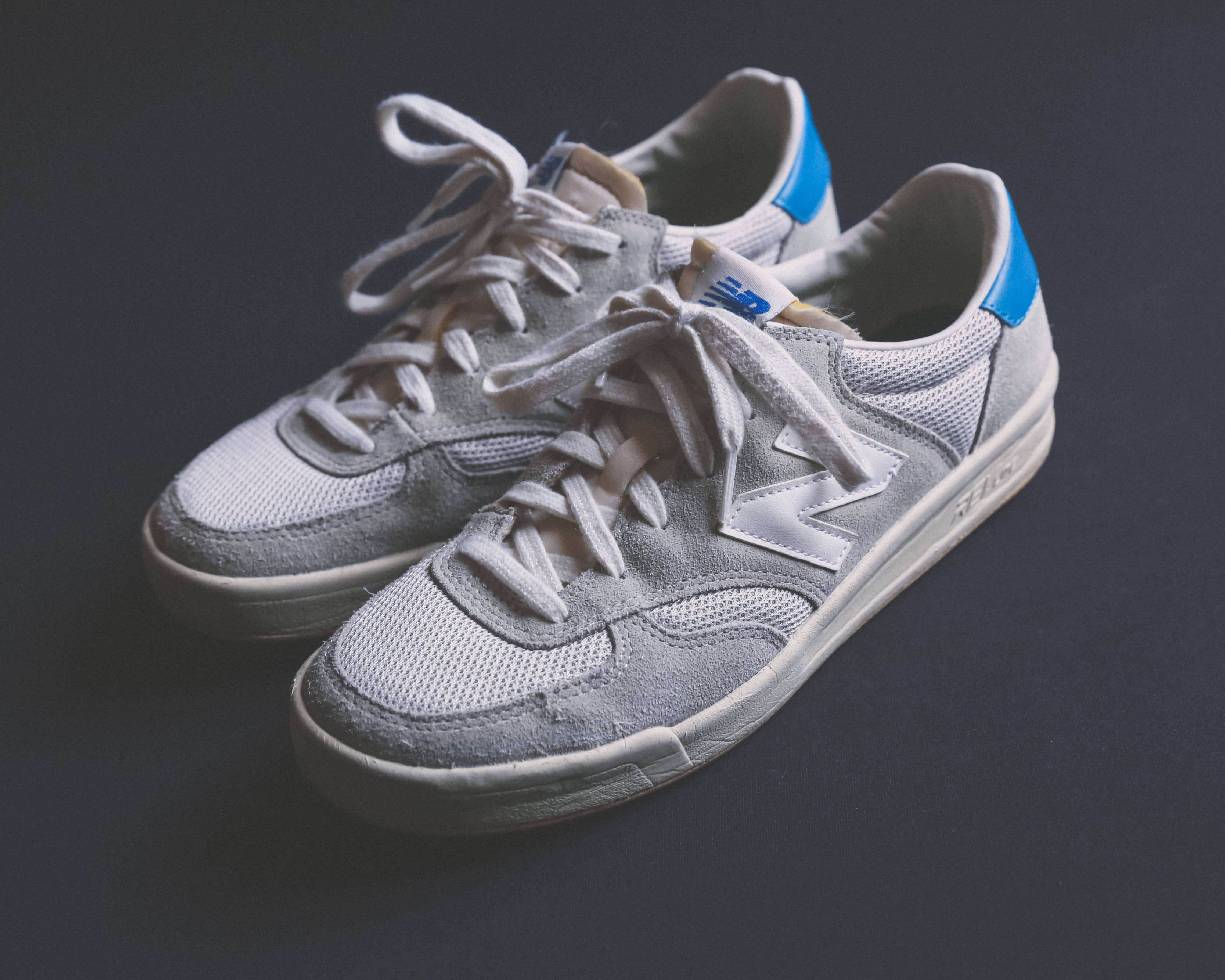 New Balance 淡色漸層鞋 壁紙 — 一對灰色 New Balance 運動鞋，帶有藍色點綴和白色鞋帶，放置在深灰色表面上。