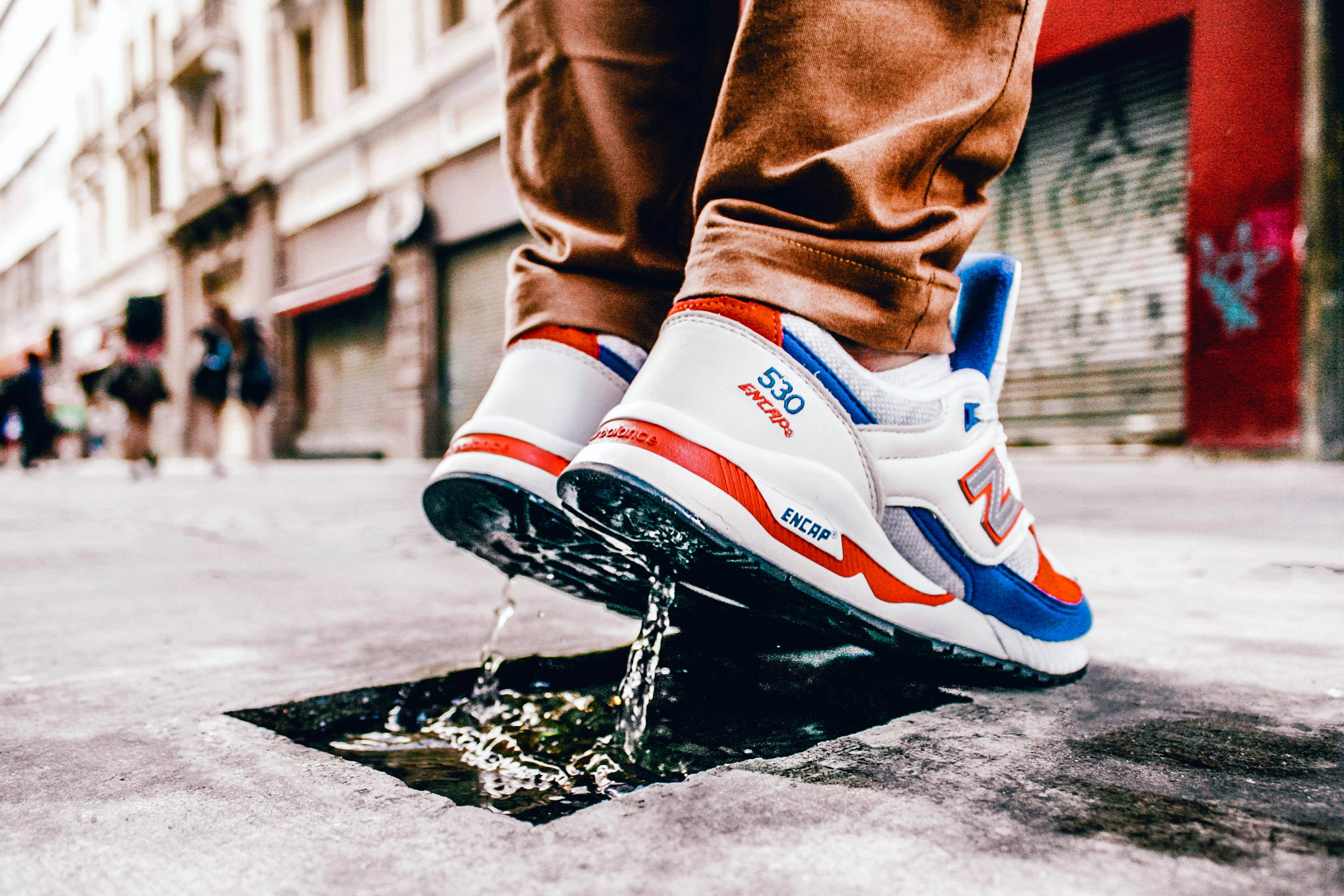 New Balance 三色鞋款 壁紙 — 鮮豔的紅、藍、白色運動鞋近距離特寫，從城市街道排水口濺起水花。