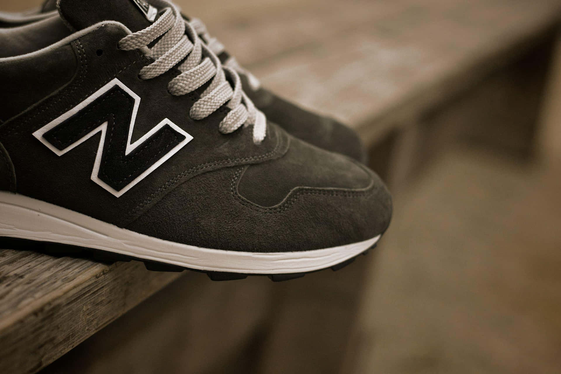 深灰色麂皮New Balance運動鞋，白色鞋帶，放在木長椅上。