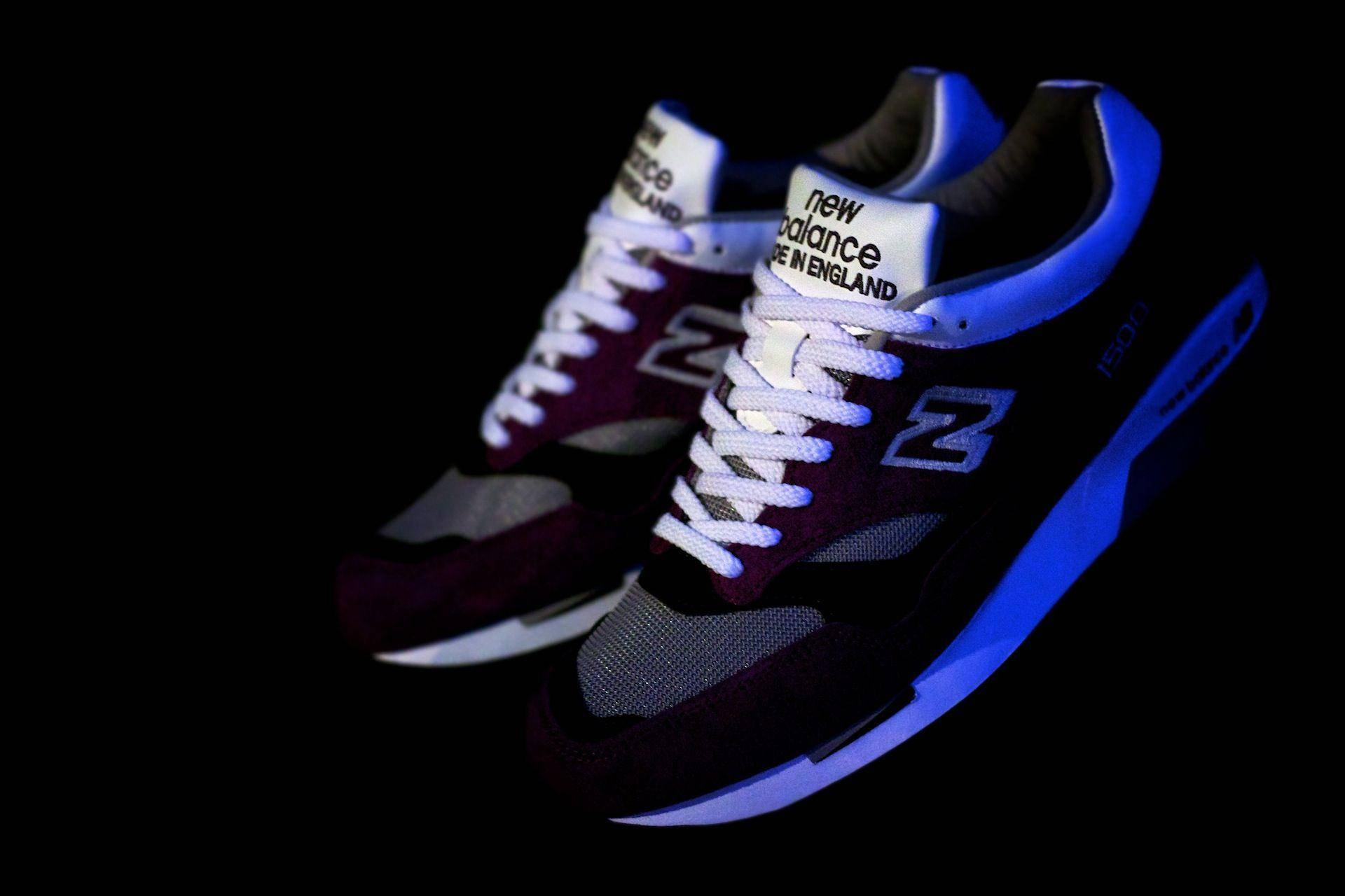 New Balance 深酒紅色調 壁紙 — 一對帶有栗色和藍色點綴的New Balance運動鞋在黑色背景的戲劇性燈光下發光。