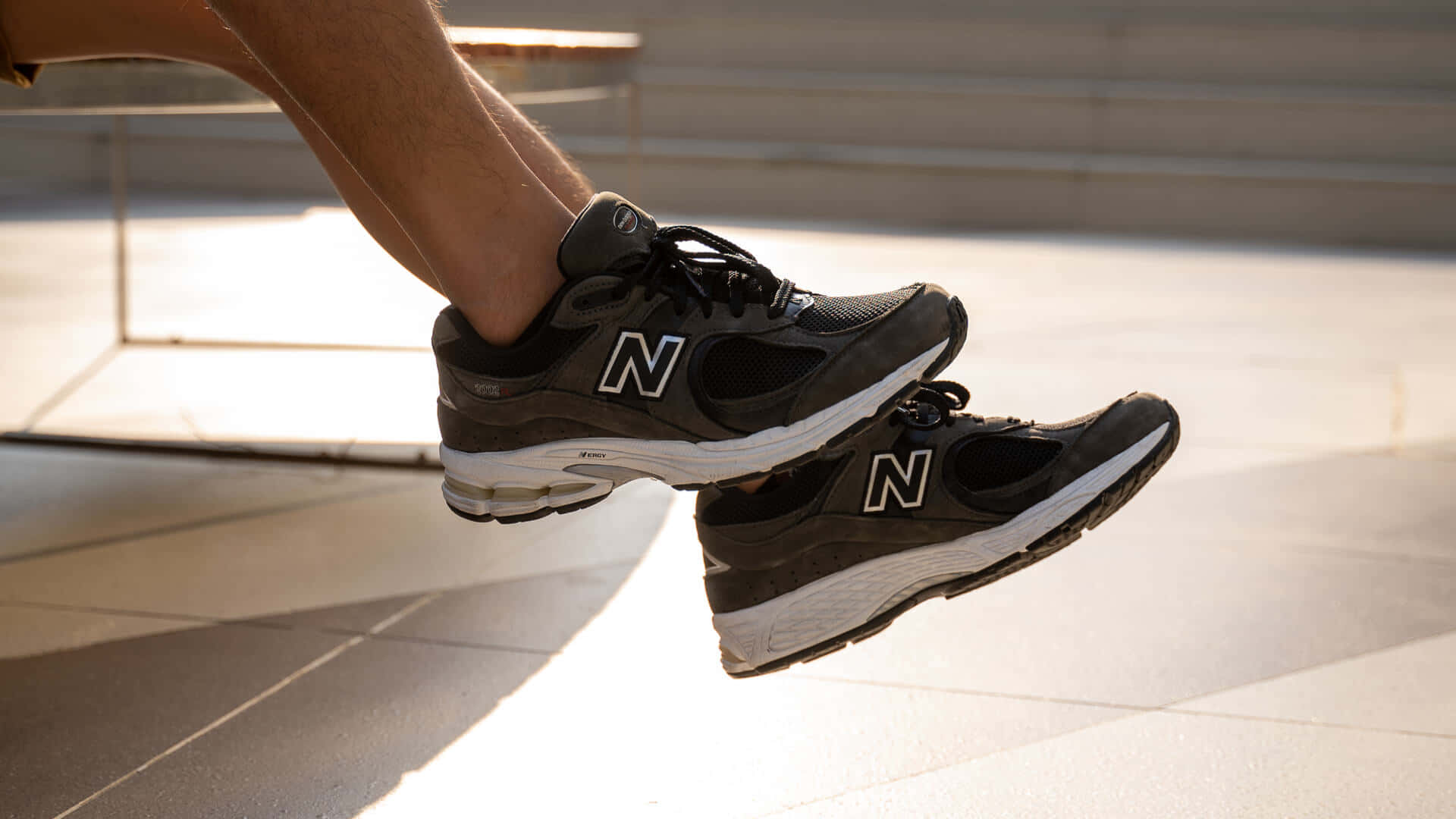 特寫鏡頭：黑色New Balance運動鞋中的腳懸浮在陽光照射的路面上方。
