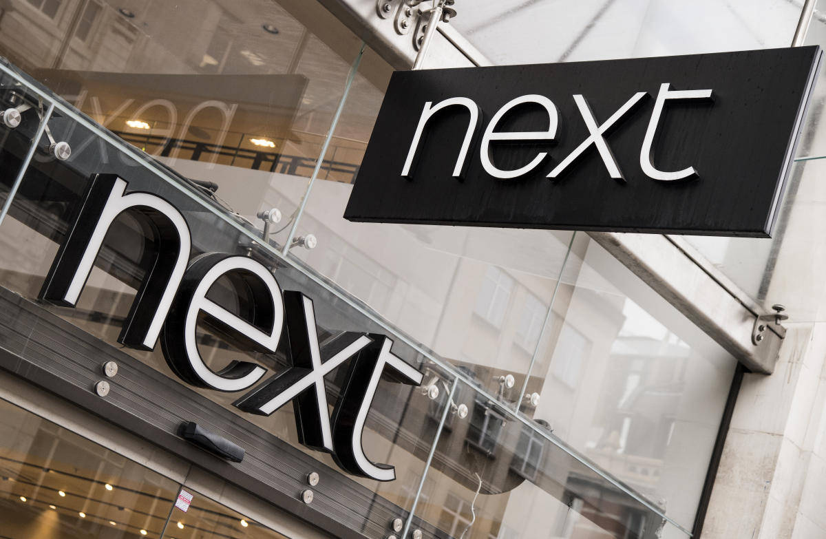 玻璃店面上的黑白「next」商店標誌，帶有城市倒影。
