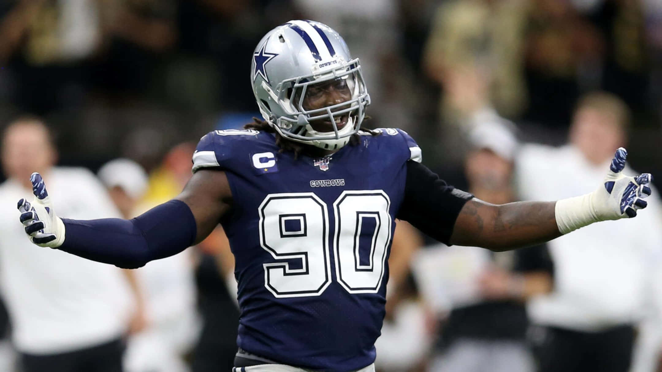 德馬庫斯·勞倫斯NFL 90號 壁紙 — 一位達拉斯牛仔隊的90號美式足球員在比賽中於球場上張開雙臂慶祝。