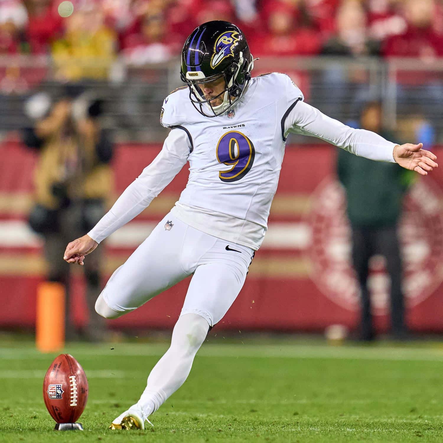 NFL 9號踢球員射門嘗試 壁紙 — 巴爾的摩烏鴉隊的踢球手身穿白色球衣，背號9號，在球場燈光下的綠色場地上踢足球。