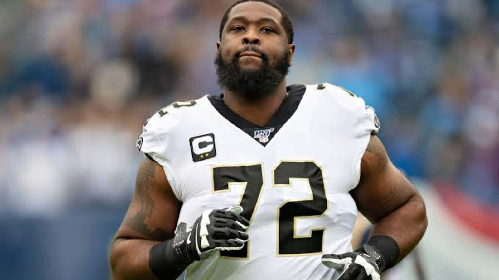 NFL 特龍·阿姆斯特德 紐奧良聖徒隊 壁紙 — 一名專注的NFL進攻截鋒身穿白色72號球衣，在比賽期間站在體育場上。