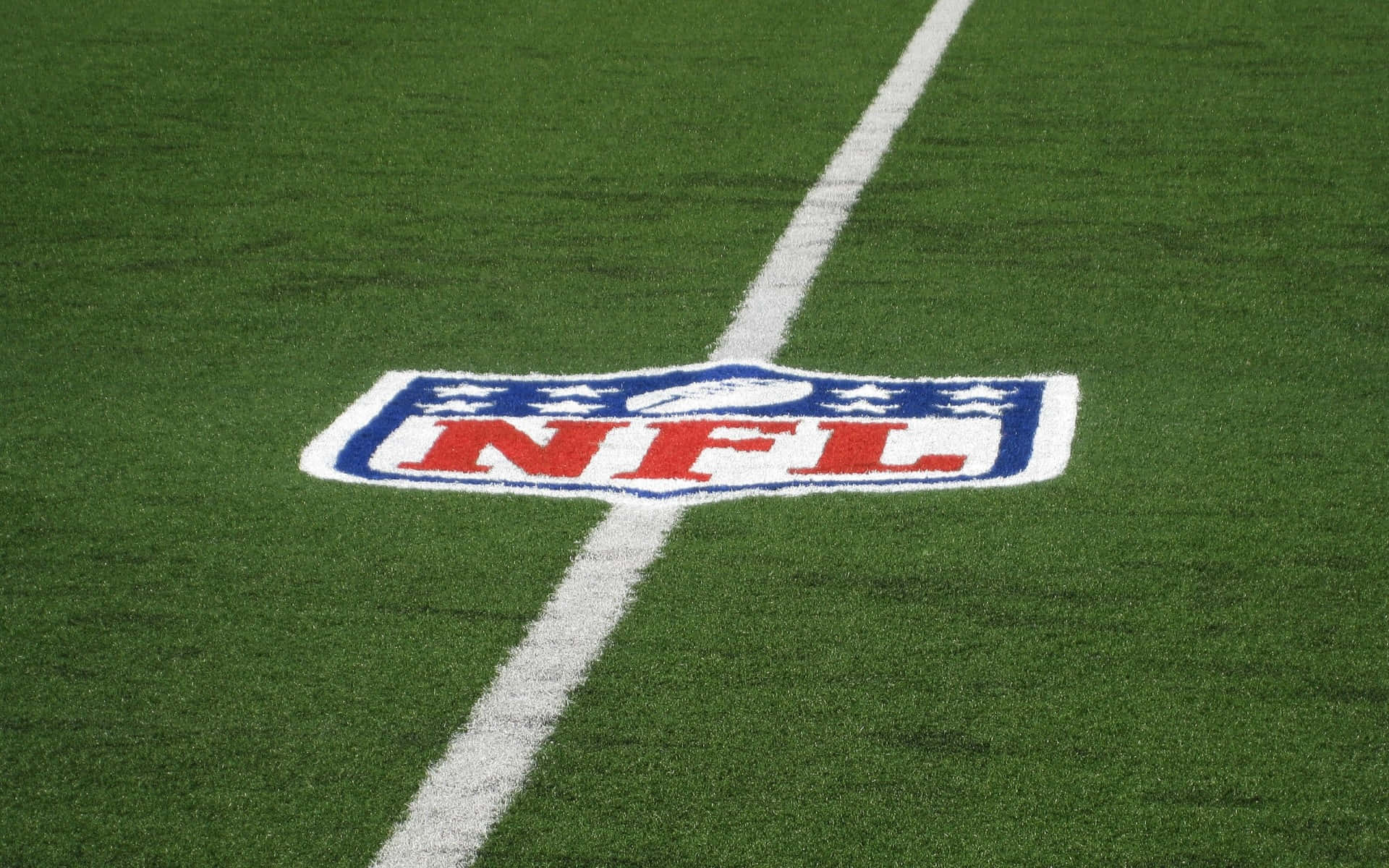 賽場焦點：NFL 賽事的緊張氛圍 壁紙 — NFL標誌的特寫，繪在充滿活力的綠色草皮上，並有一條清晰的白色碼線與之交錯。