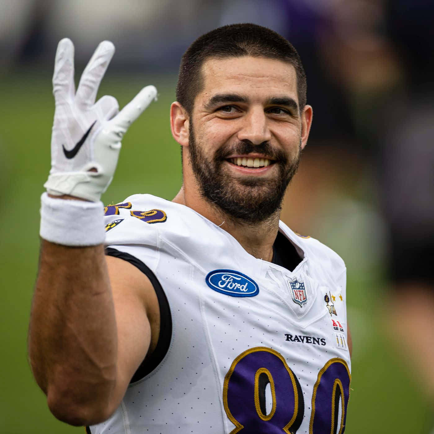 馬克·安德魯斯NFL球員 壁紙 — 一位微笑的NFL球員身穿白色烏鴉隊球衣，戴著手套的手揮舞著，伸出兩根手指。