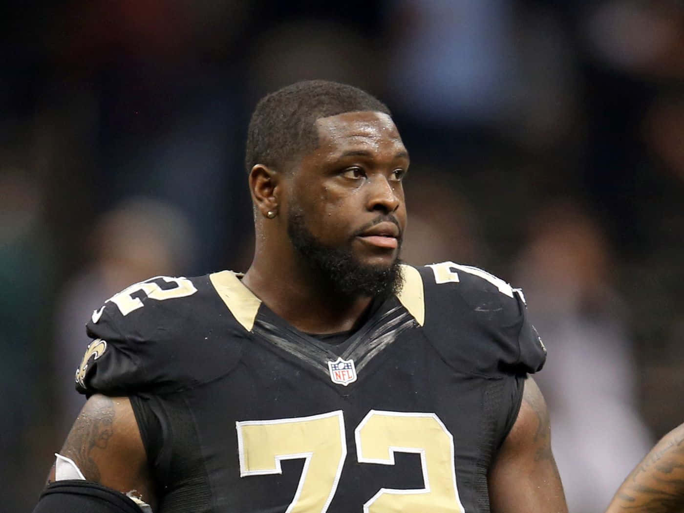 NFL Offensive Tackle 特龍·阿姆斯特德 新奧爾良聖徒隊 壁紙 — 比賽中，一名專注的NFL球員身穿黑色和金色球衣，號碼73的特寫。
