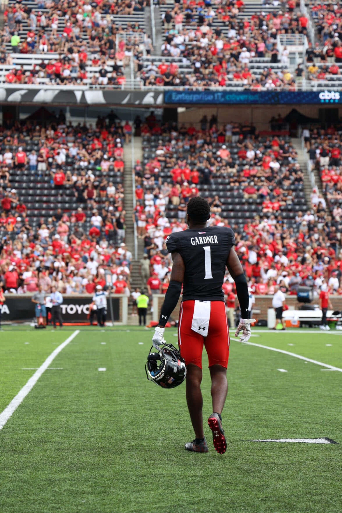 阿馬德·加德納 NFL 預賽步行 壁紙 — 一名身穿一號球衣的足球員背對鏡頭走過綠色球場，身後是坐滿紅衣球迷的體育場。