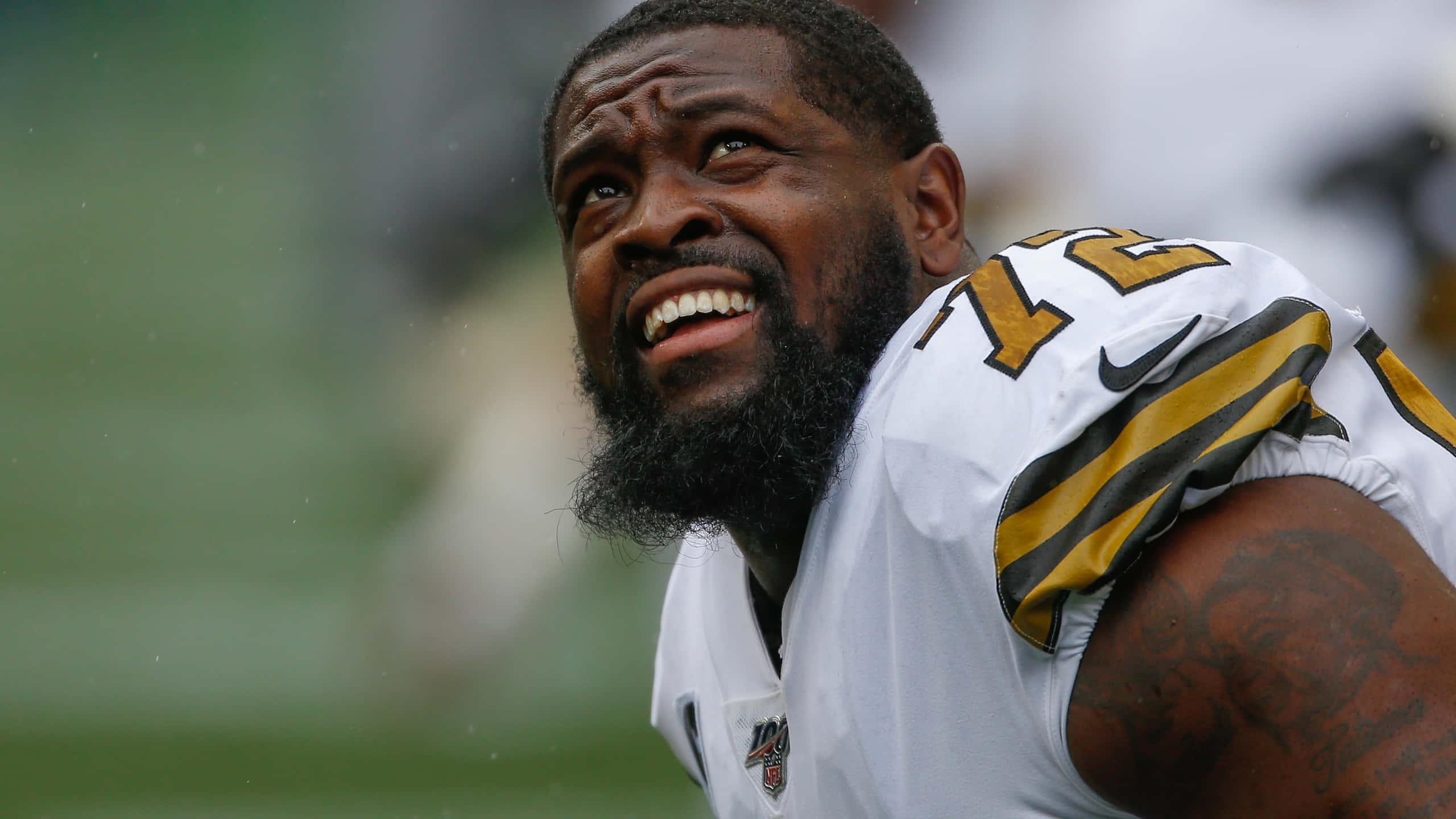 特龍·阿姆斯特德 新奧爾良聖徒隊 NFL 球員 壁紙 — 一位鬍鬚足球員身穿白色金色球衣，在雨中的球場上大笑的特寫。