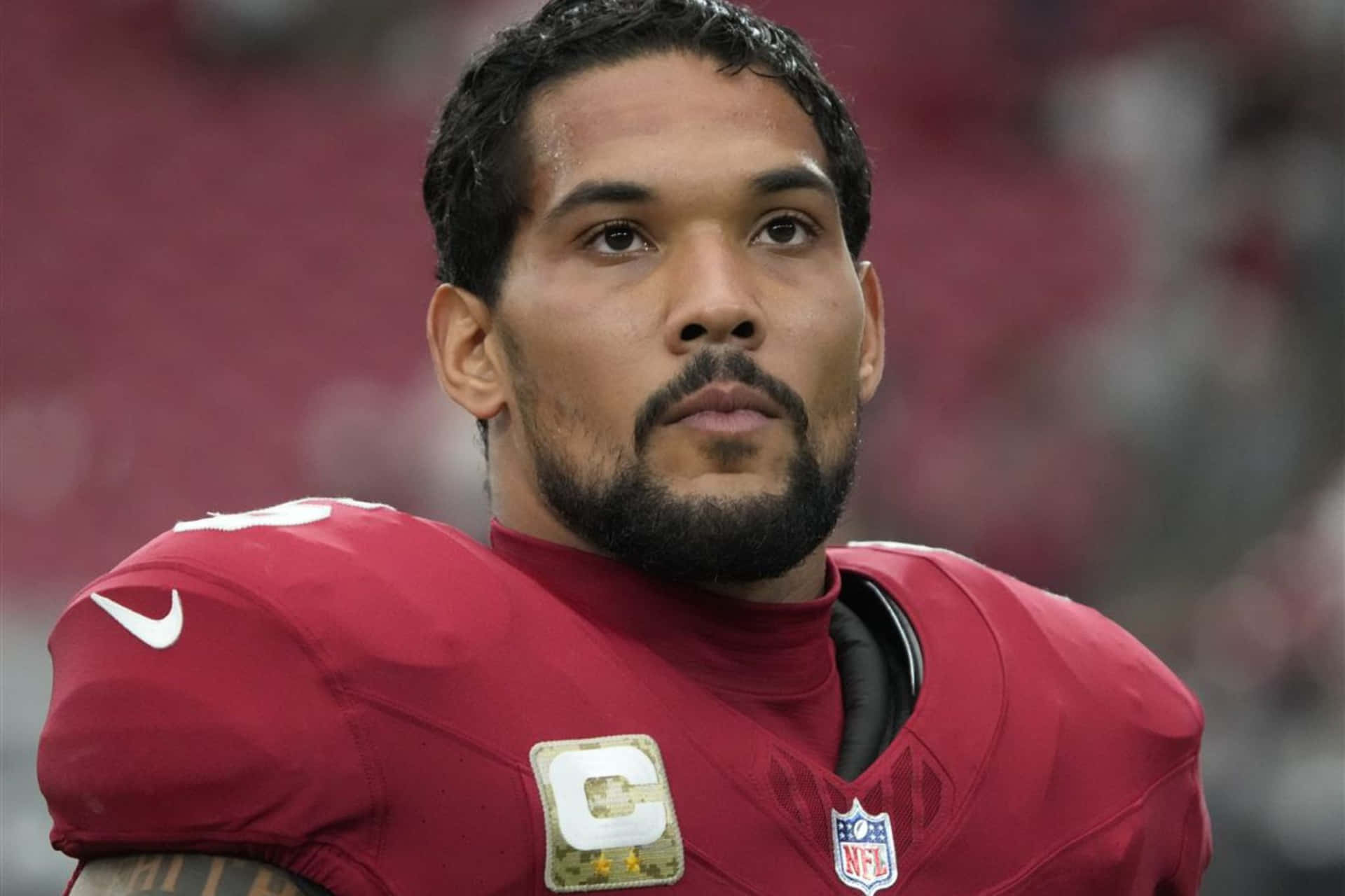  壁紙 — 一位身穿紅色球衣、帶有隊長臂章嘅NFL球員，喺球場燈光下嘅比賽中專注地凝視。