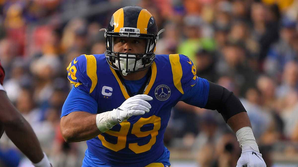 NFL 亞倫·唐納德奔跑於足球場 壁紙 — 一名專注的NFL防守截鋒身穿藍金色公羊隊球衣，在日間比賽中衝刺，身後是模糊的體育場人群。