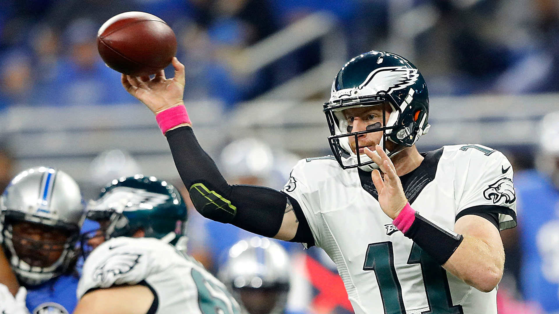 NFL 卡森·溫茲持球 壁紙 — 費城老鷹隊的四分衛身穿白色11號球衣，在NFL日間比賽中準備傳球，背景有隊友和模糊的體育場。