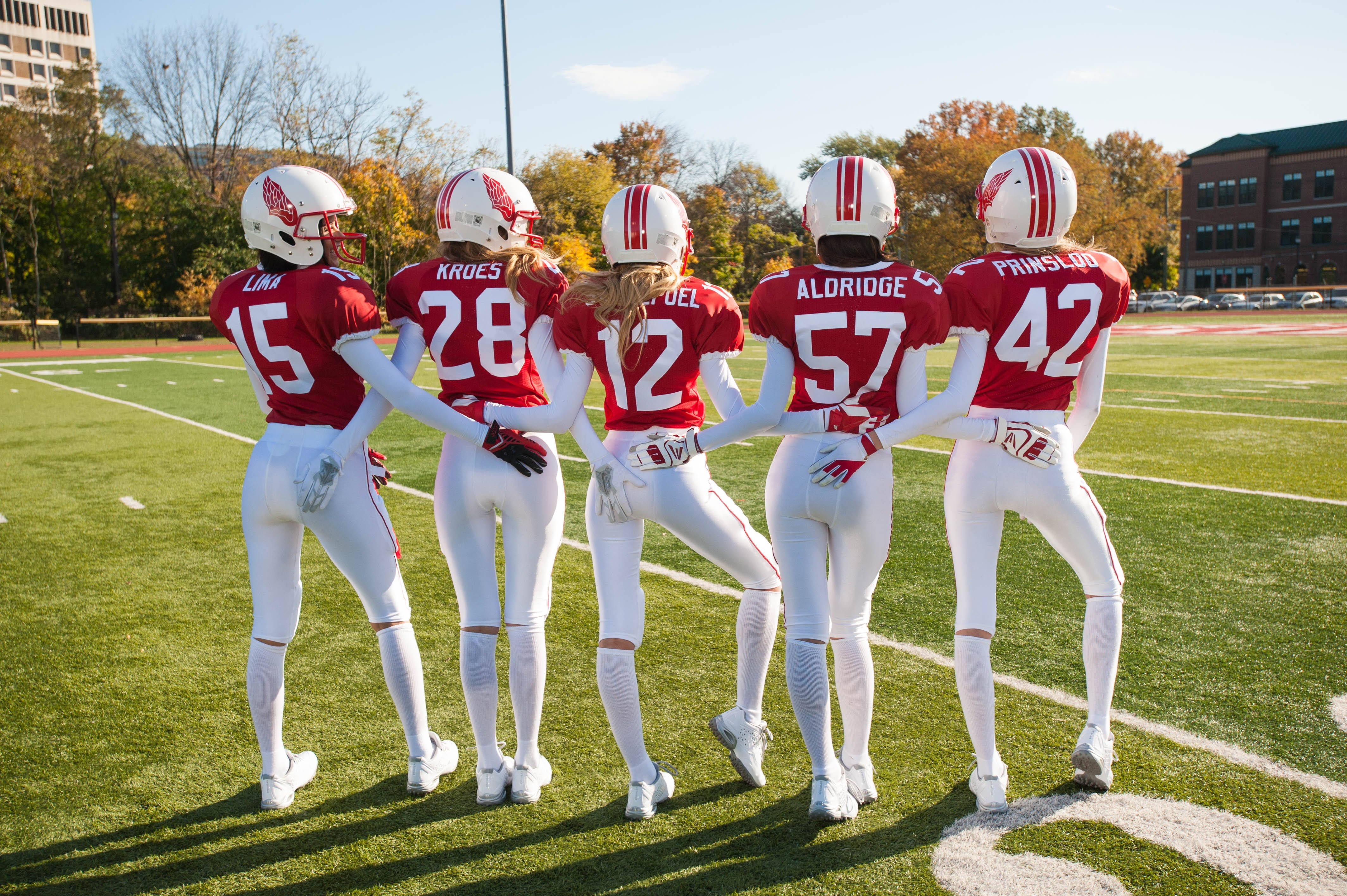 NFL 女性足球模特 壁紙 — 五名身穿紅白球衣的女足球員在陽光明媚的球場上站在一起，背景是秋天的樹木。