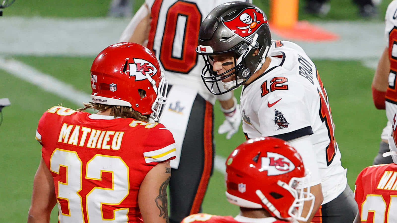 身穿紅白球衣的NFL美式足球員在夜間的綠色場地上。