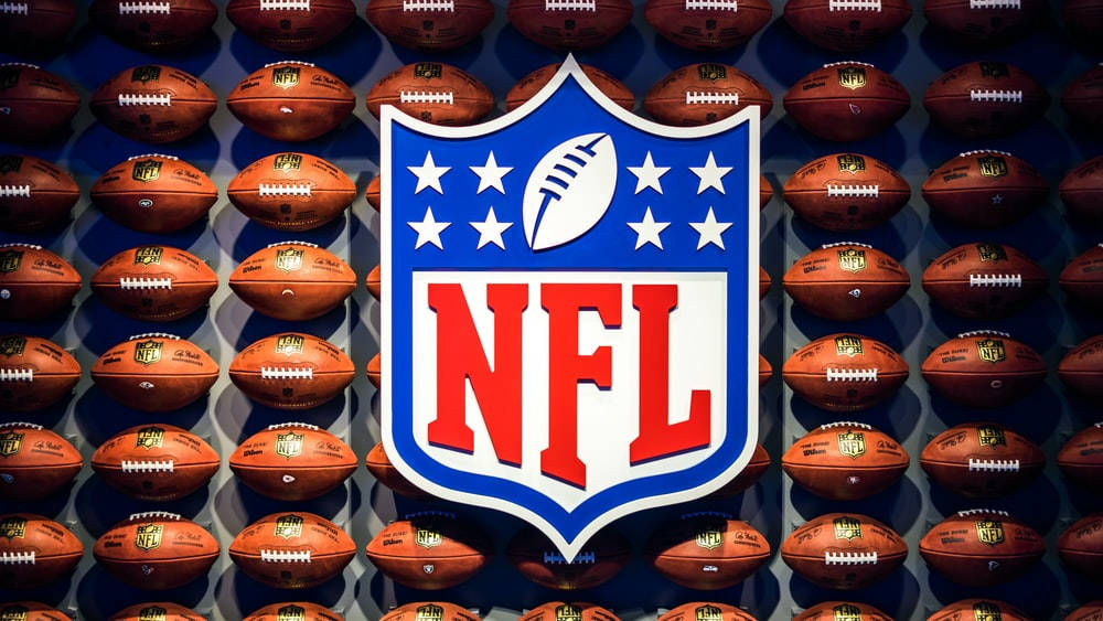 NFL 標誌與足球 壁紙 — NFL 標誌置中於棕色美式足球牆上，在明亮的攝影棚燈光下。