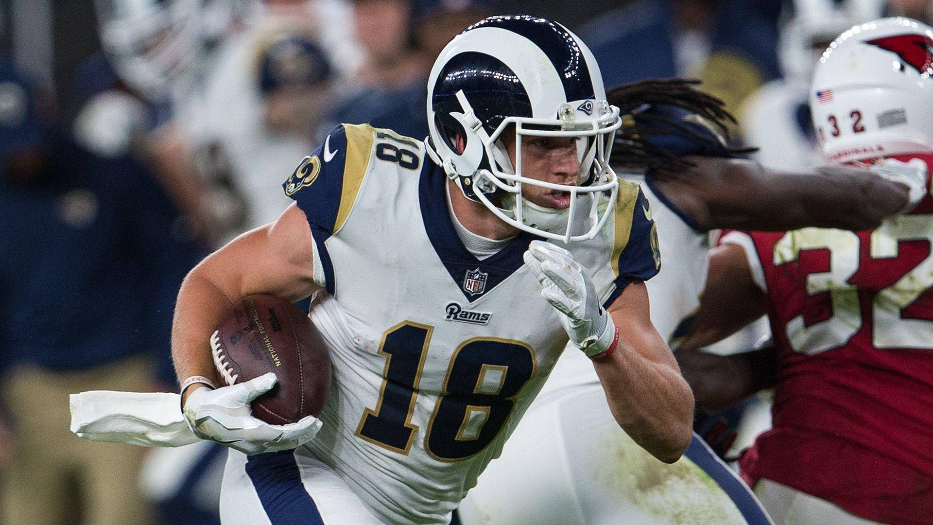 NFL 洛杉磯公羊隊的庫珀·庫普 壁紙 — 一名身穿白色和金色球衣的洛杉磯公羊隊美式足球員帶球奔跑，同時被一名身穿紅色的對方球員追趕。