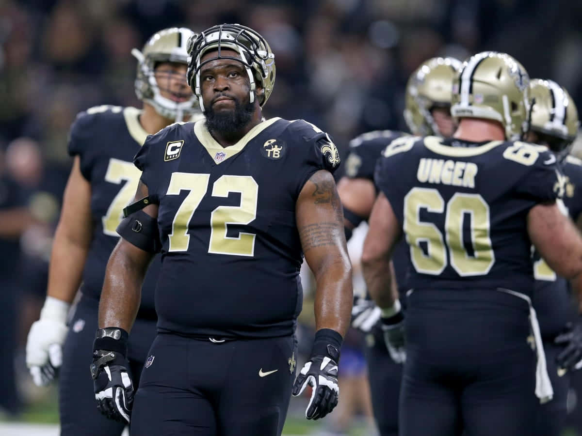 NFL 球員 特龍·阿姆斯特德 新奧爾良聖徒隊 壁紙 — 一位專注的新奧爾良聖徒隊美式足球員，身穿72號球衣，在比賽中站在場上，背景有隊友。