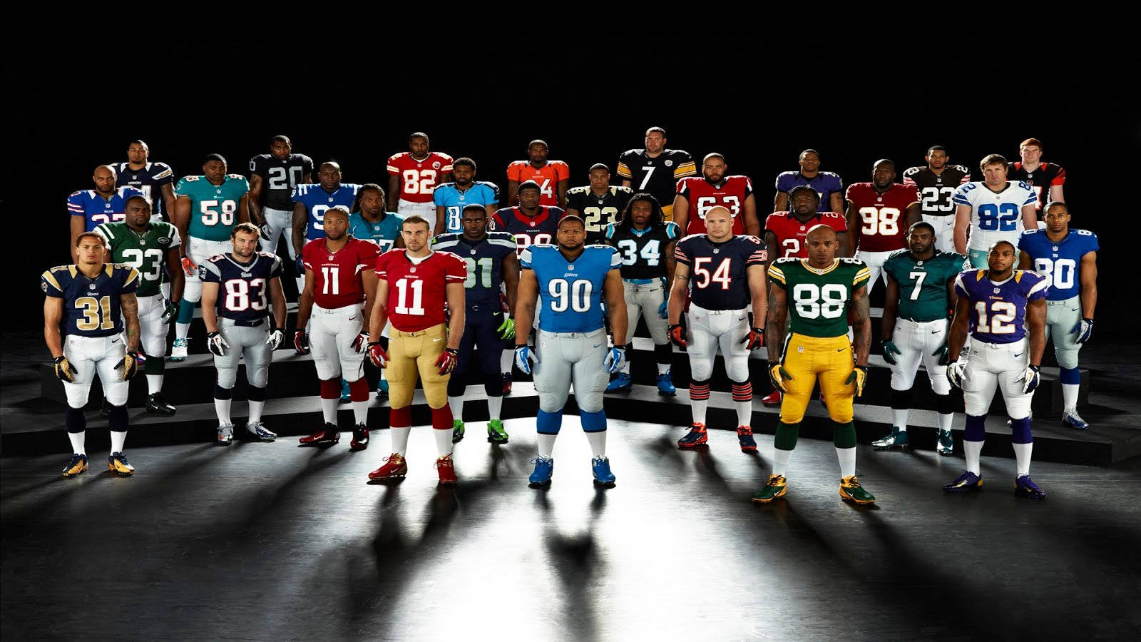 NFL 球隊代表 壁紙 — 職業美式足球運動員身穿隊服，在黑暗的舞台上於戲劇性的聚光燈下排成隊形。