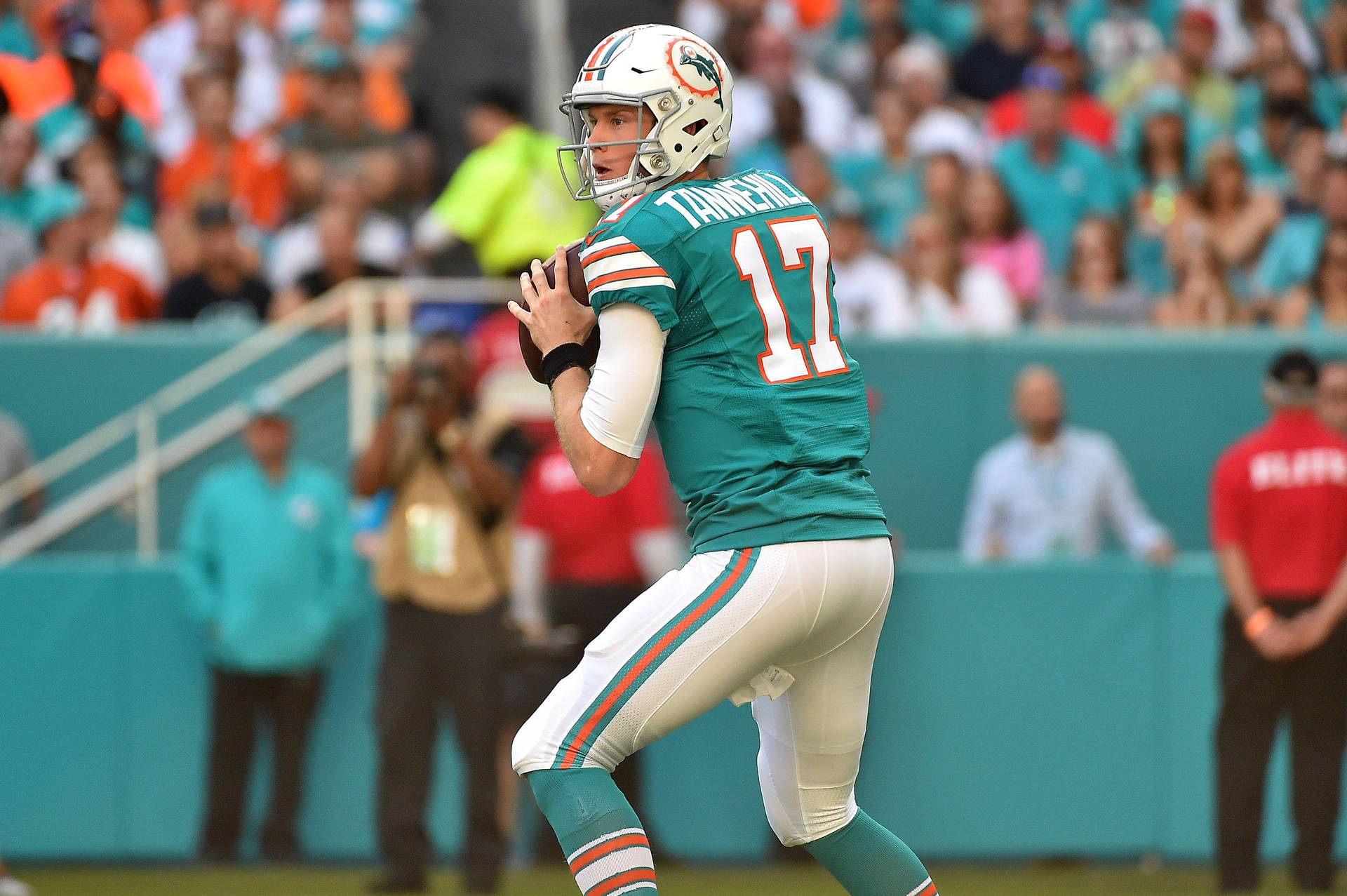 NFL外卡賽瑞安·坦尼爾 壁紙 — 邁阿密海豚隊四分衛Ryan Tannehill身穿青綠色和白色球衣，在日間比賽中準備傳球，背景有球迷。
