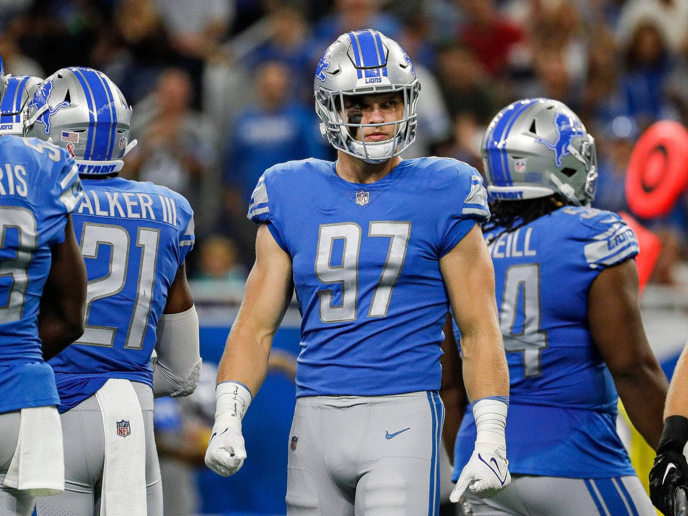 NFL底特律獅隊97號艾登·哈欽遜 壁紙 — 底特律雄獅隊的足球員身穿藍色和銀色制服，在比賽期間帶著專注的表情走進球場。