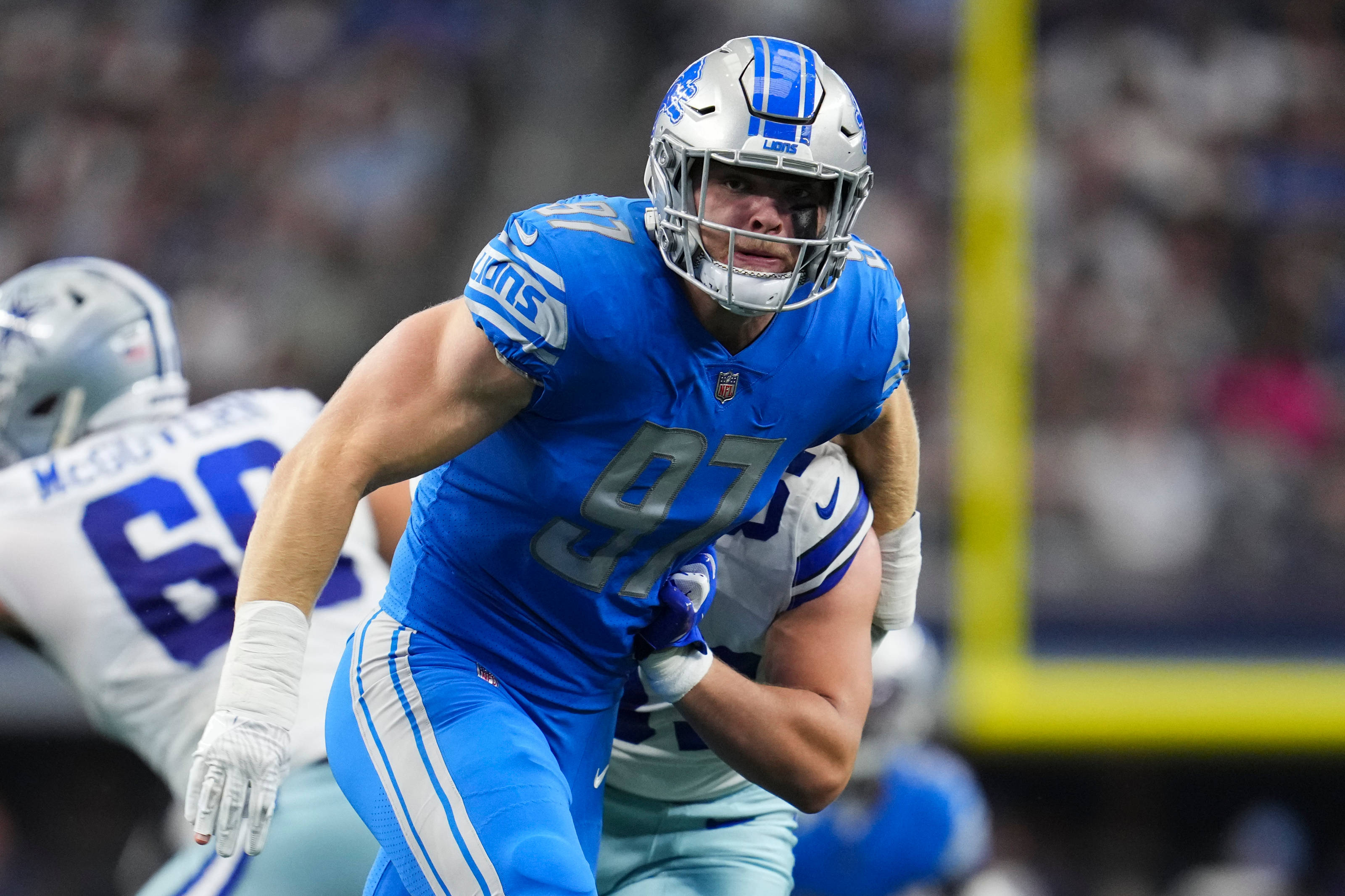 NFL底特律獵鷹隊艾丹·漢遜 壁紙 — 底特律雄獅隊的藍色制服美式足球員在夜間比賽中，於球場燈光下擒抱對手。