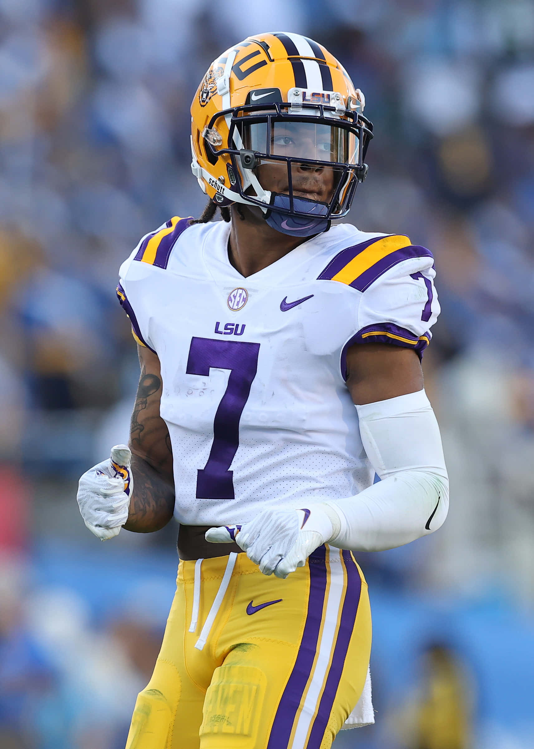 NFL新秀明星德里克·辛格利 Jr. 壁紙 — 一名專注的LSU美式足球員身穿白色、紫色和金色球衣，在陽光普照的球場上奔跑，背景是模糊的體育館人群。