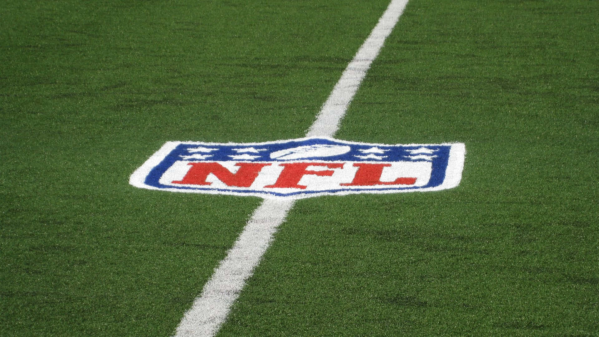 Football Stadium 桌布 壁紙 — NFL標誌的特寫，繪在充滿活力的綠色草地上，被一條清晰的白色碼線穿過。