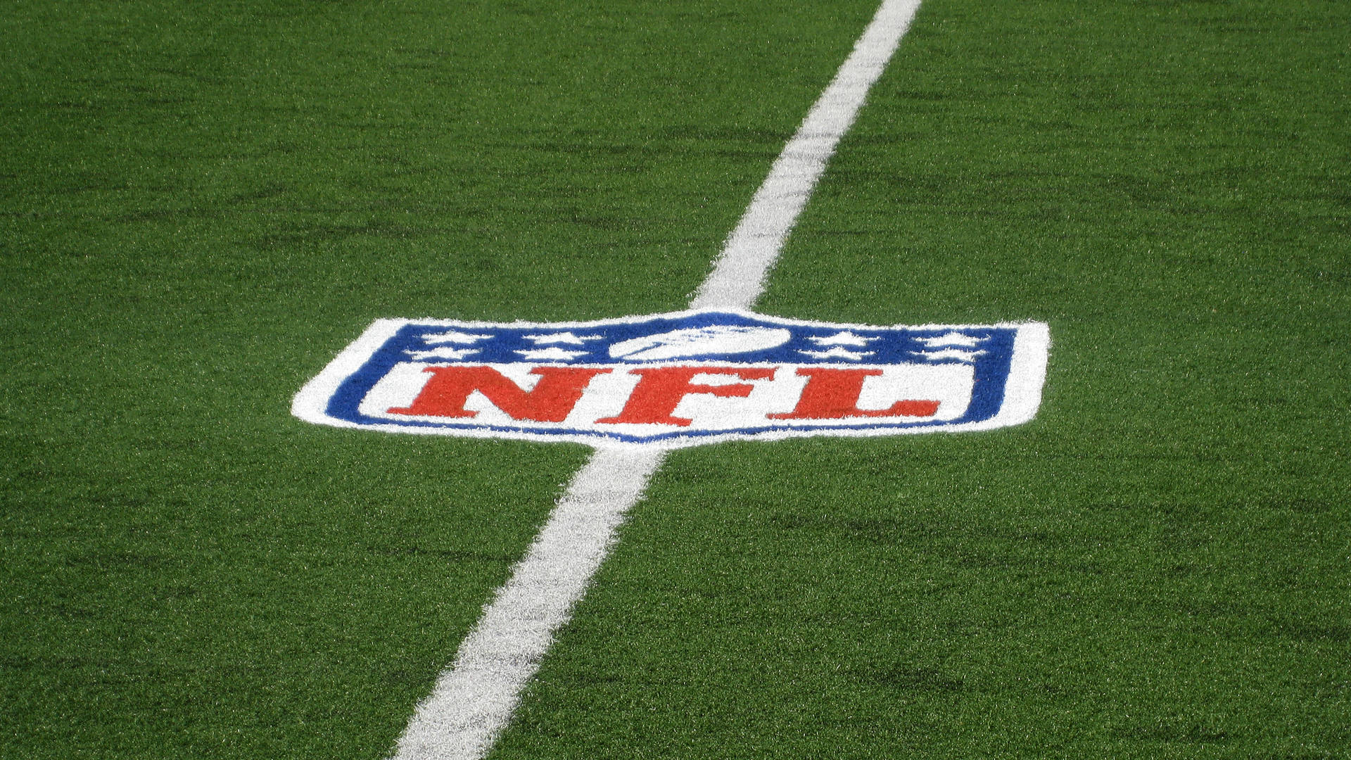 NFL標誌置於球場中央 壁紙 — NFL標誌的特寫，繪在充滿活力的綠色草地上，被一條清晰的白色碼線穿過。