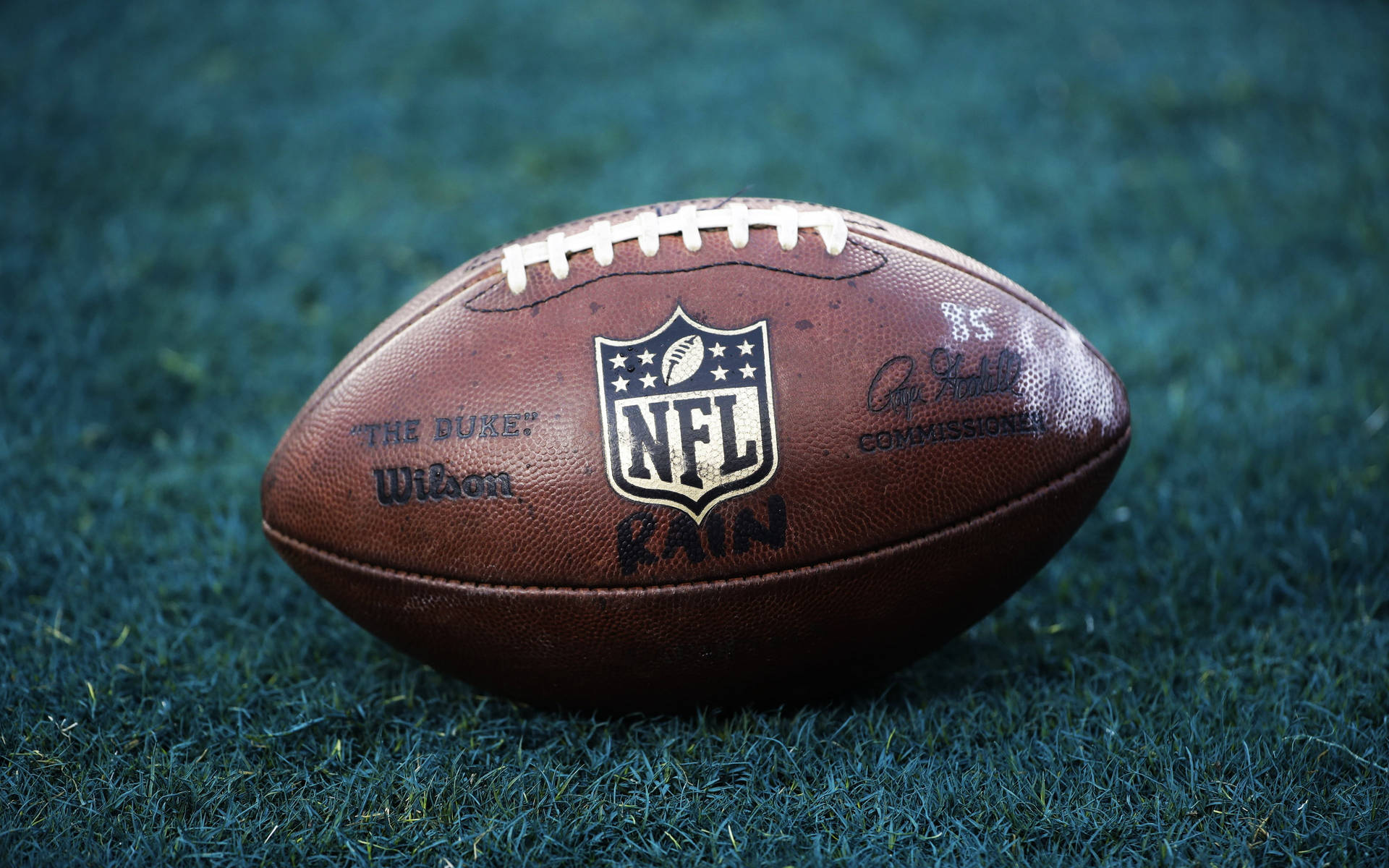 一個棕色NFL橄欖球在綠色草地上，可見鞋帶和標誌。