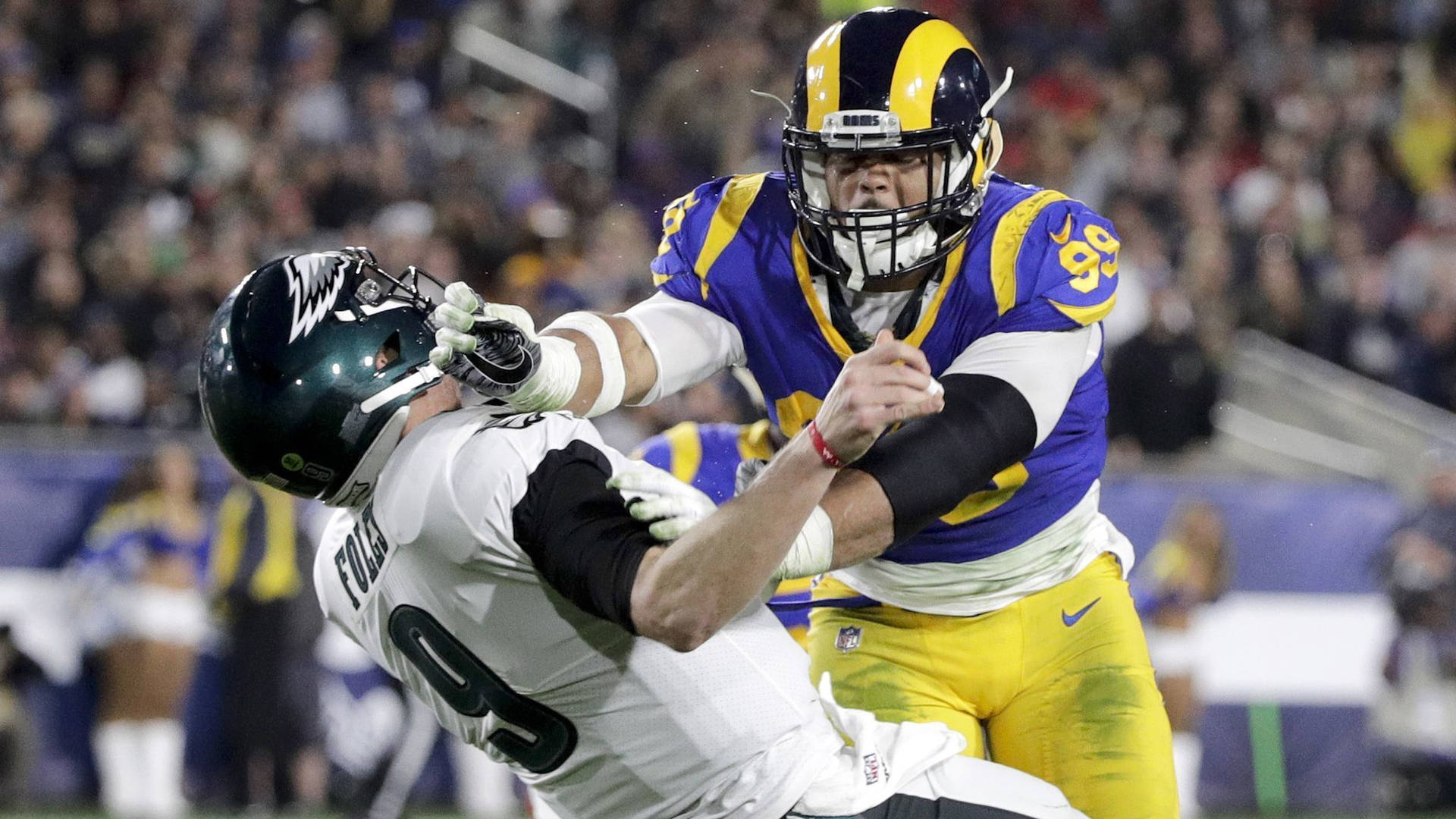 NFL比賽 亞倫·唐納德與尼克·福勒斯 壁紙 — 洛杉磯公羊隊的防守球員在夜間美式足球比賽中擒抱費城老鷹隊的四分衛。
