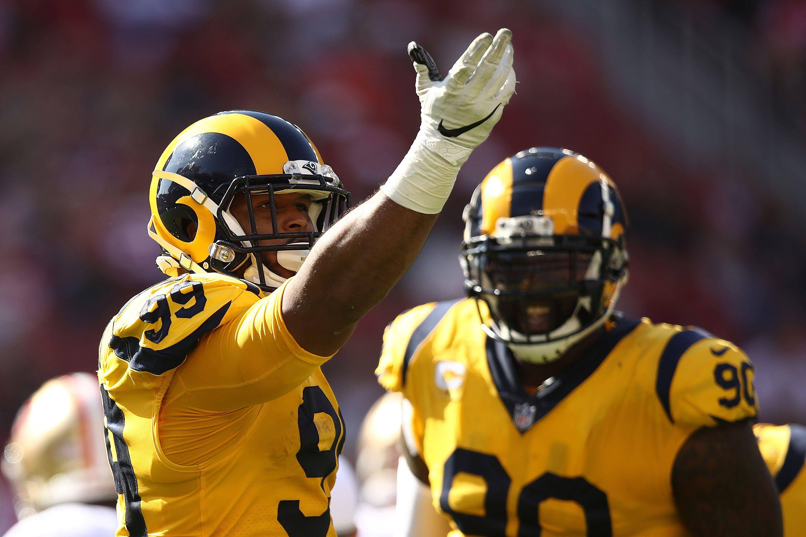 NFL比賽阿隆·唐納德黃色球衣 壁紙 — 兩名身穿黃色球衣的洛杉磯公羊隊美式足球員在陽光明媚的日間比賽中向球迷揮手。