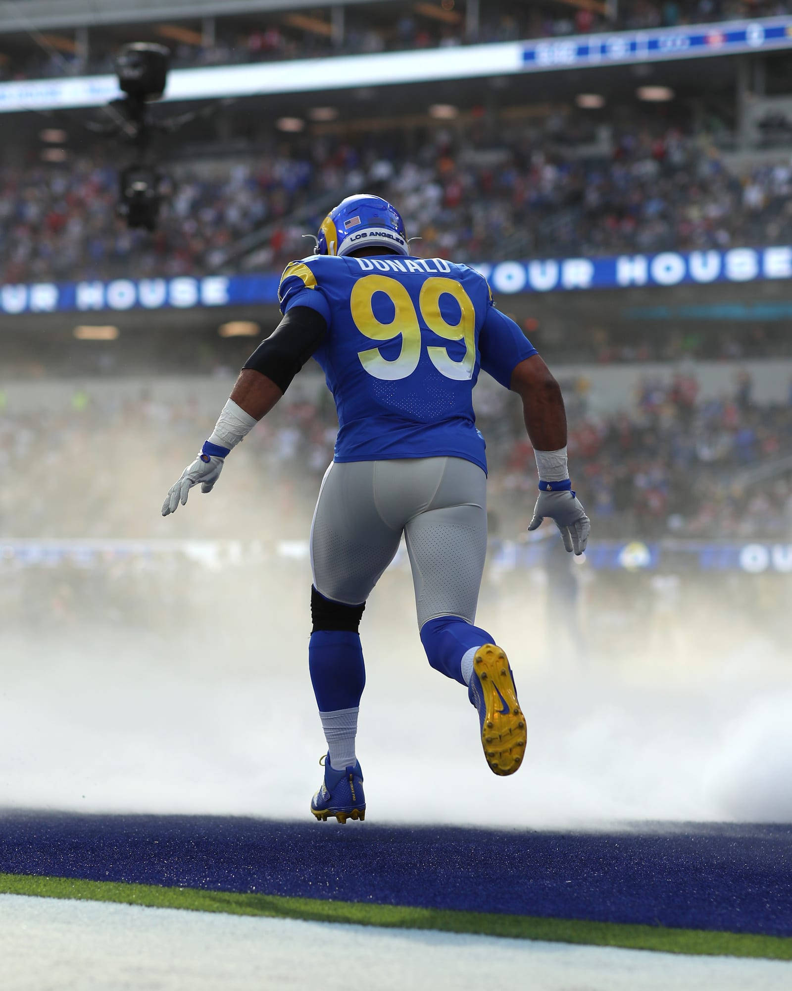NFL洛杉磯公羊隊亞倫·唐納德足球賽事 壁紙 — 一名身穿藍色球衣、號碼99的足球員穿過煙霧瀰漫的體育場隧道跑向球場。